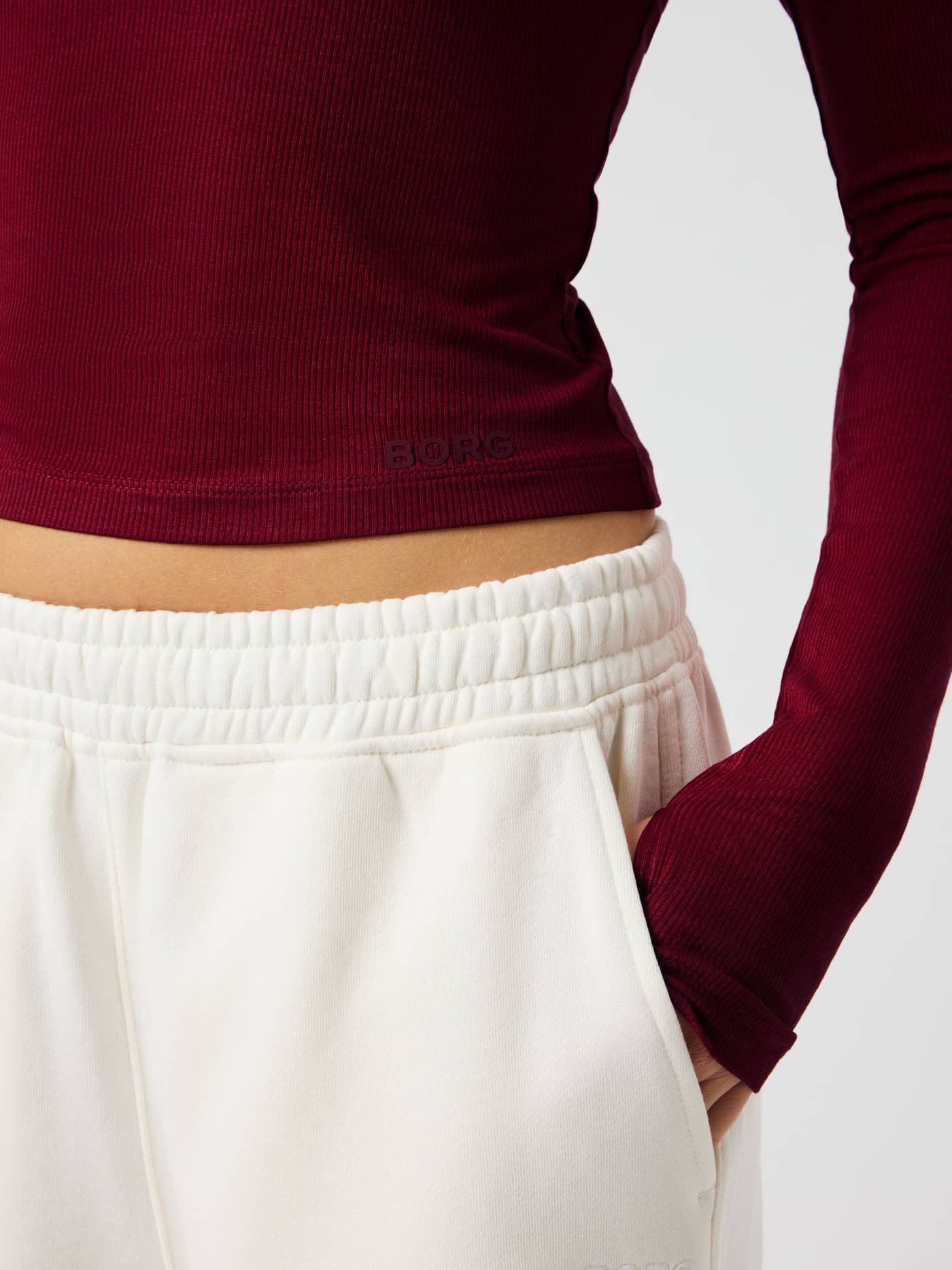 Närbild på Studio Ribbed Cropped Long Sleeve i Cabernet (röd) som visar det nedre trycket framtill och det ribbade tyget. - Image 6