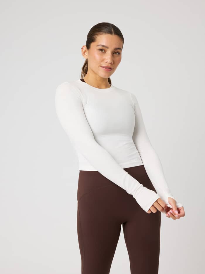 Studio Ribbed Cropped Long Sleeve in Tofu (Wit) met duimgaten en trainingsdesign, vooraanzicht bij een vrouw.