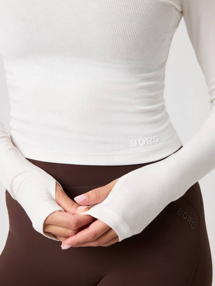 Close-up van de Studio Ribbed Cropped Long Sleeve in Tofu (Wit), met duimgaten en print op de voorkant.
