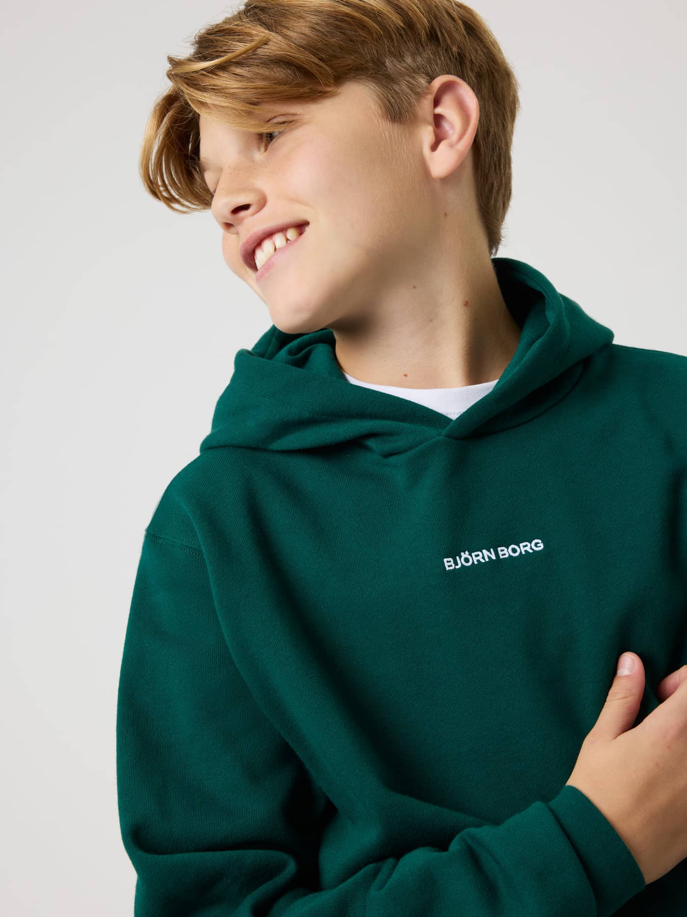 Close-up of the kids' Borg Classic Hoodie in Rain Forest (Green) with white logo embroidery on the chest. - Image 4