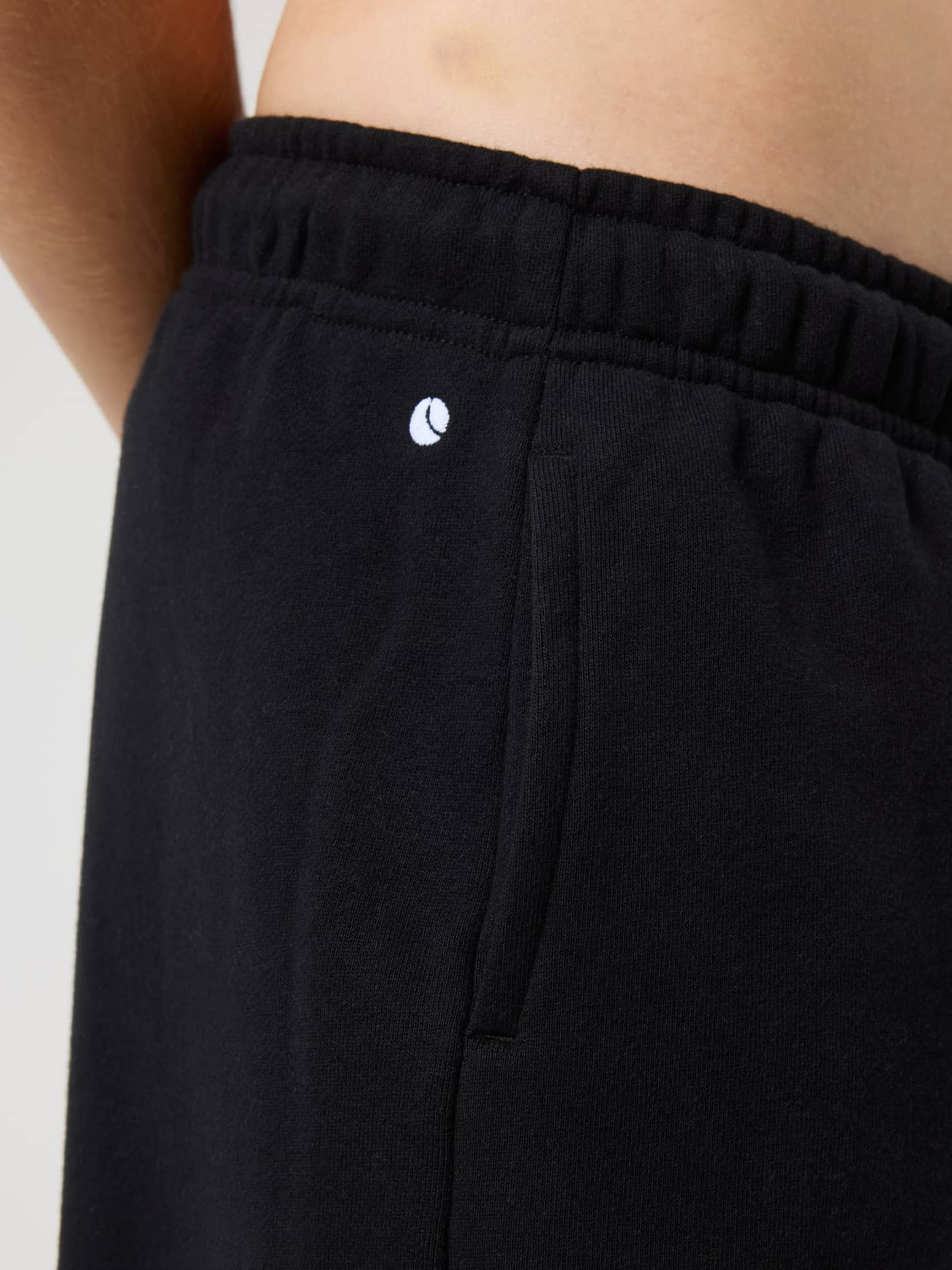Close-up of the kids Borg Classic Sweatpants in Black Beauty (Black) with a side pocket and white tennis logo. - Image 5