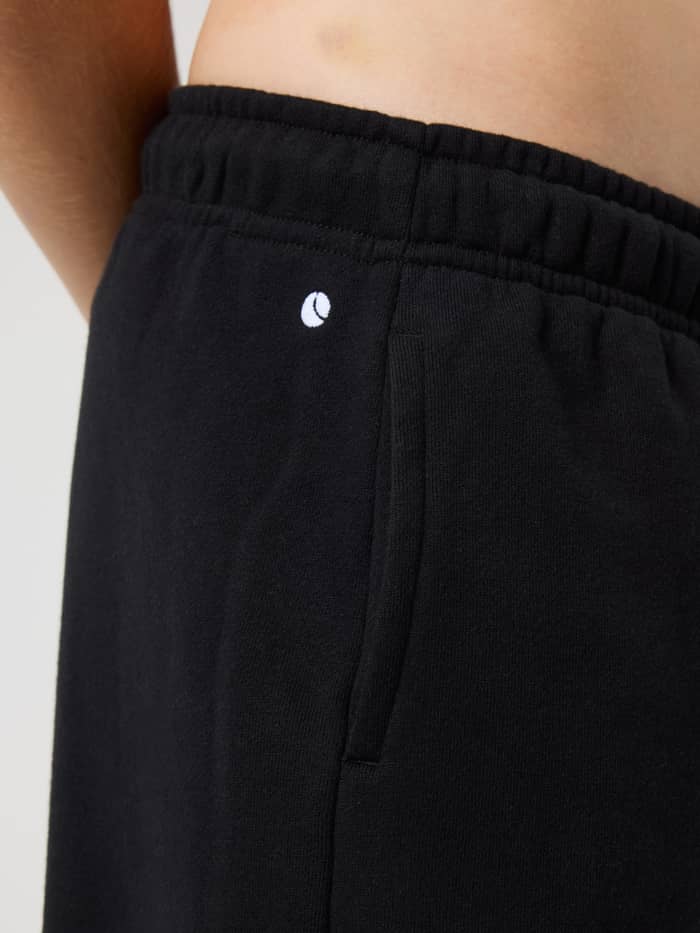 Close-up of the kids Borg Classic Sweatpants in Black Beauty (Black) with a side pocket and white tennis logo. - Image 5
