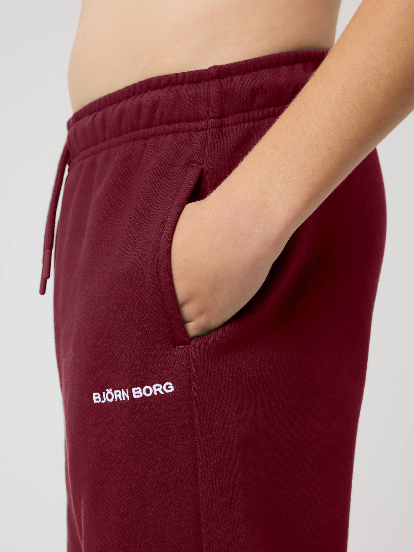 Close-up of the Borg Classic Sweatpants in Cabernet (Red) featuring side pockets, a drawstring waist, and logo embroidery. - Image 4