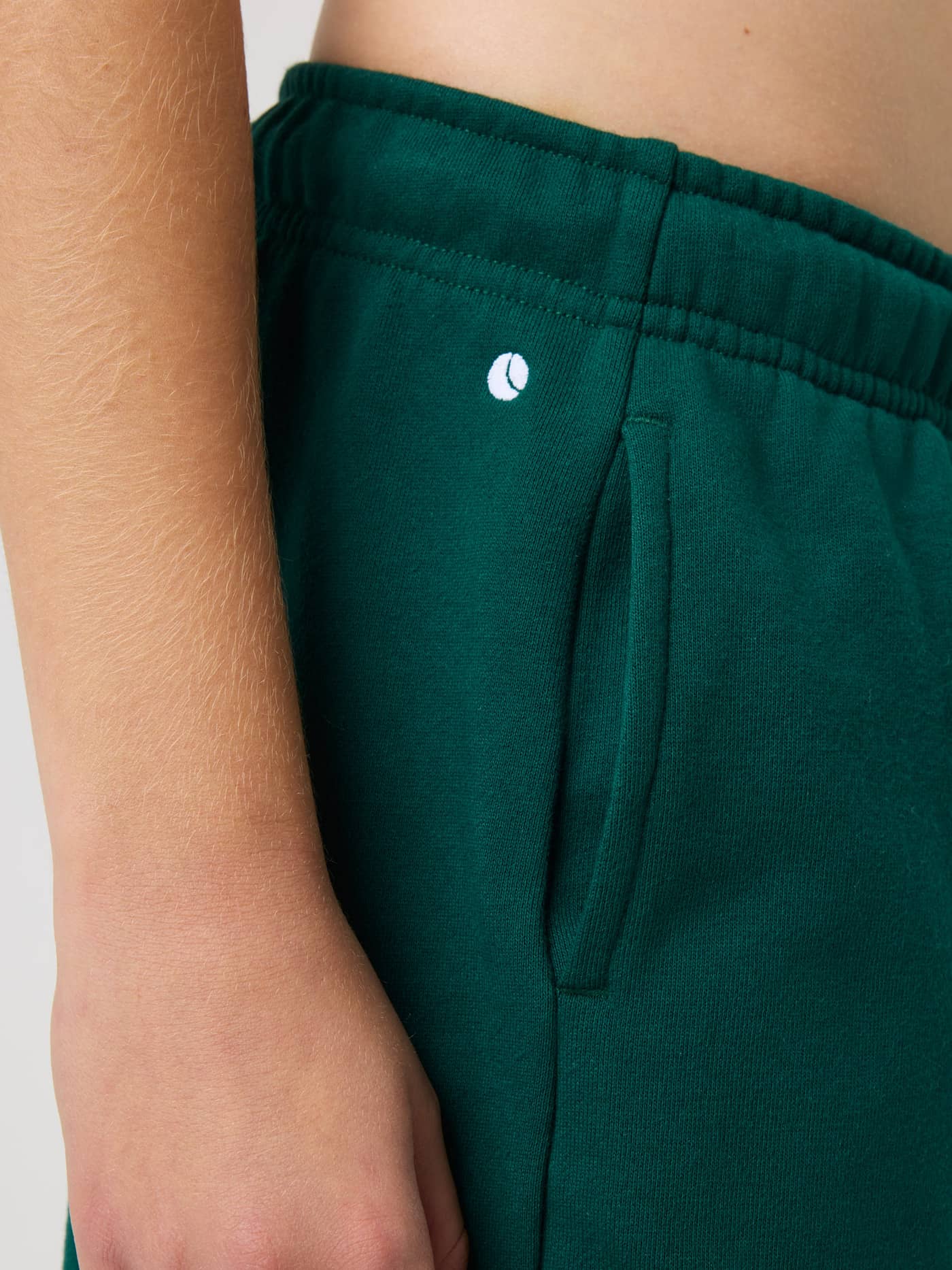 Close-up of kids' Borg Classic Sweatpants in Rain Forest (Green) featuring a white tennis logo and side pocket. - Image 5