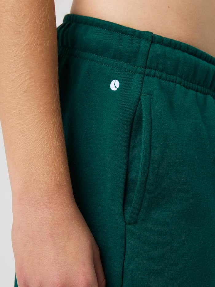Close-up of kids' Borg Classic Sweatpants in Rain Forest (Green) featuring a white tennis logo and side pocket. - Image 5