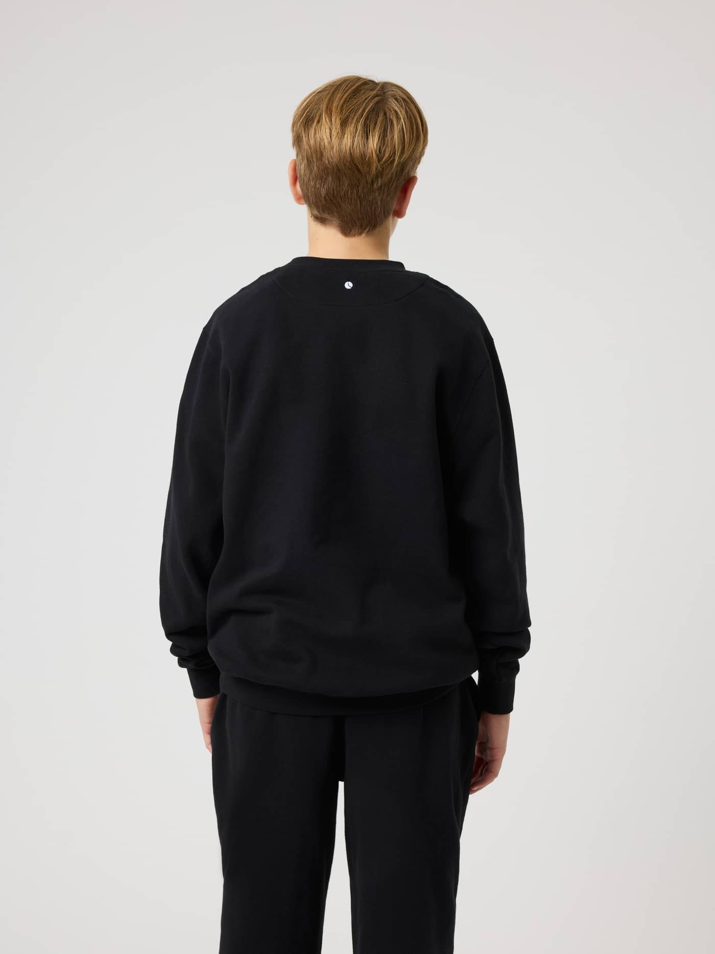 Back view of a kid in the Borg Classic Sweatshirt in Black Beauty (Black) with a small white logo at the back neck. - Image 2