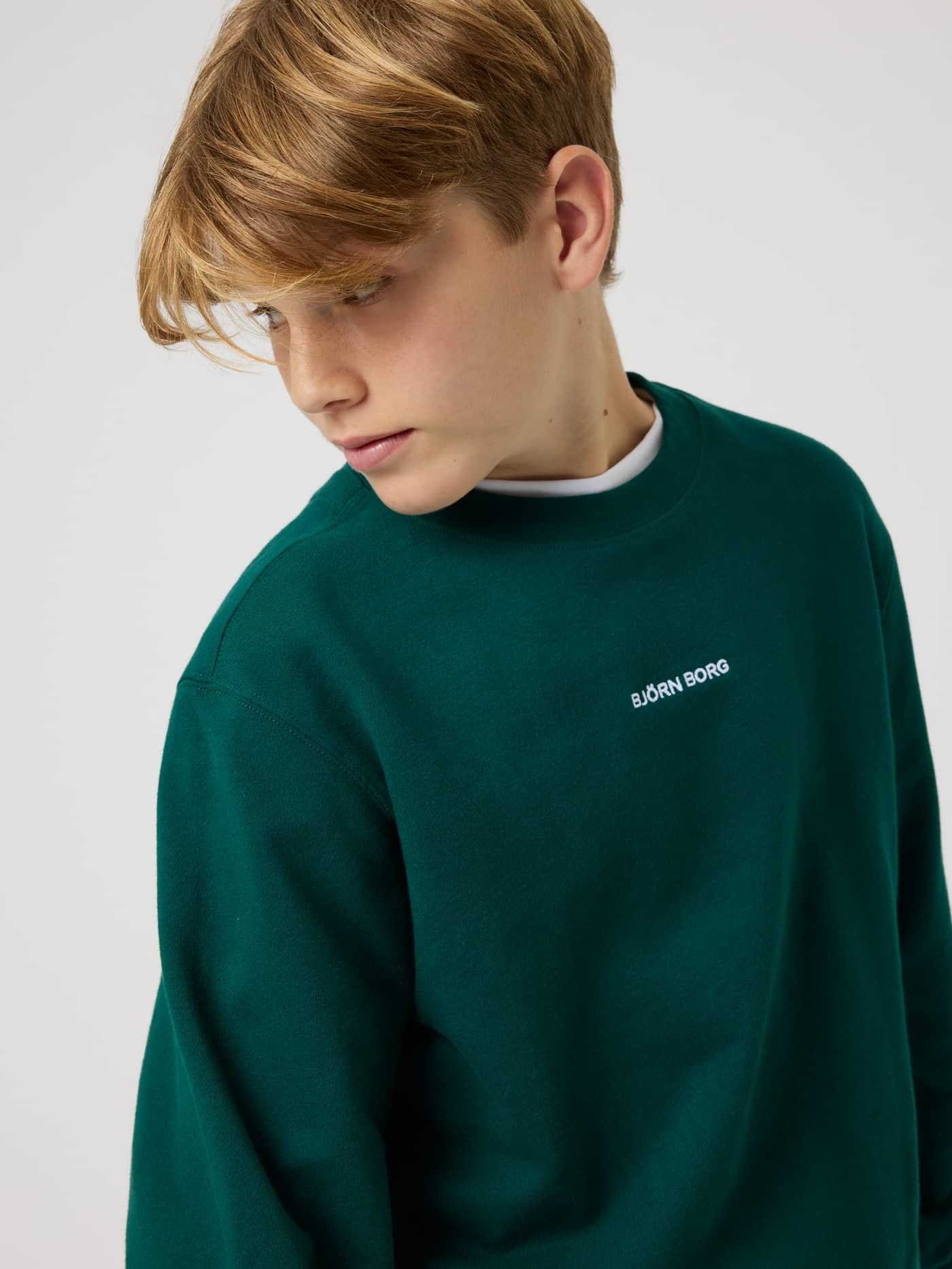 Side view of a kid wearing the Borg Classic Sweatshirt in Rain Forest (Green) with white logo and tennis-inspired style. - Image 4