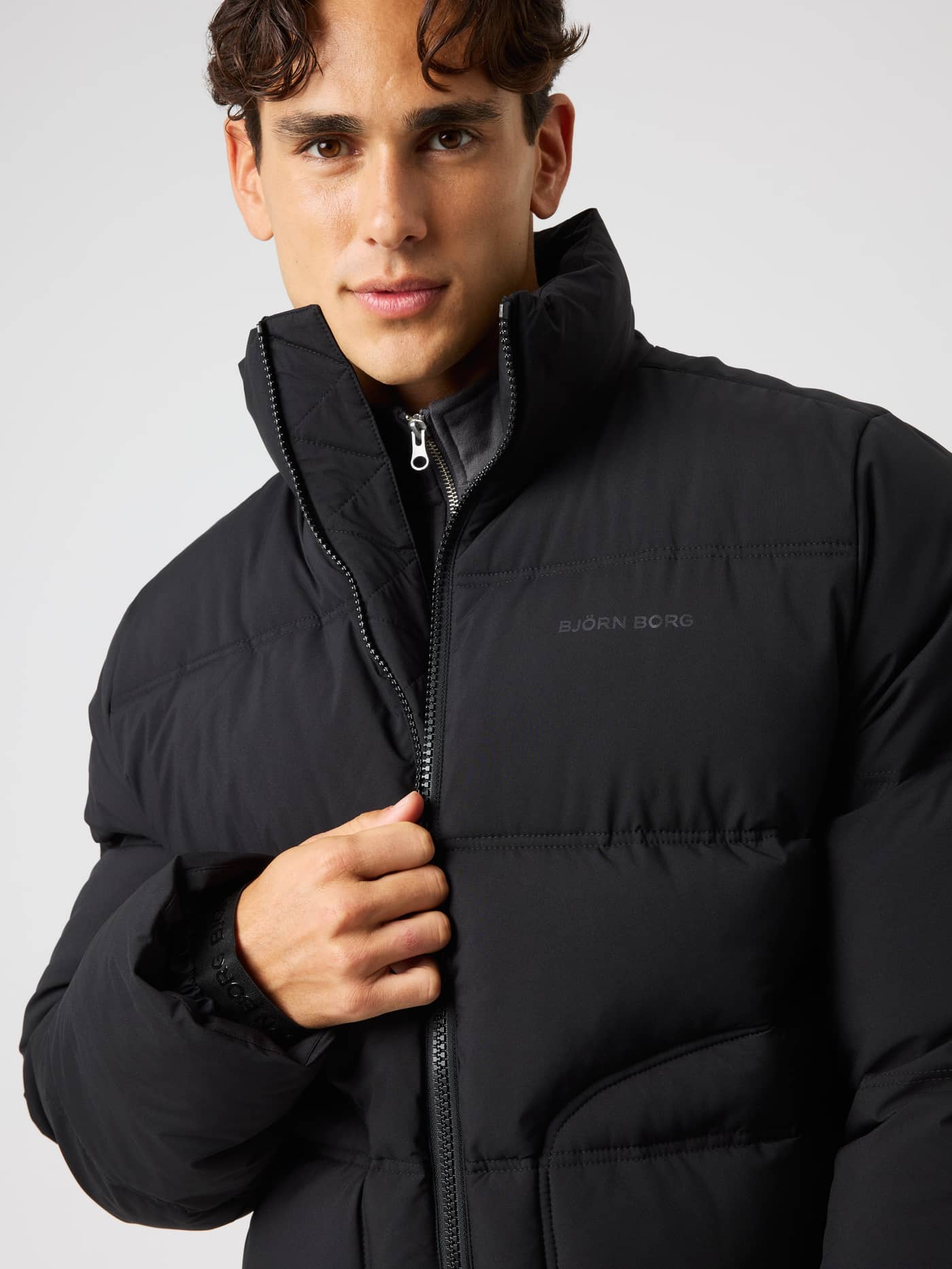 Nærbilde av vattert Borg Puffer Jacket i Black Beauty (Svart) med ton-i-ton-logo og høy krage for bevegelse. - Image 5