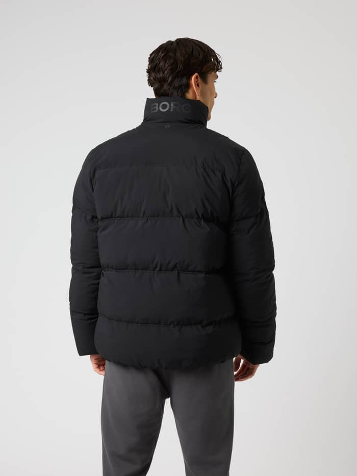 Back view of a model wearing the Borg Puffer Jacket in Black Beauty (Black) with a padded design and tonal collar logo. - Image 2