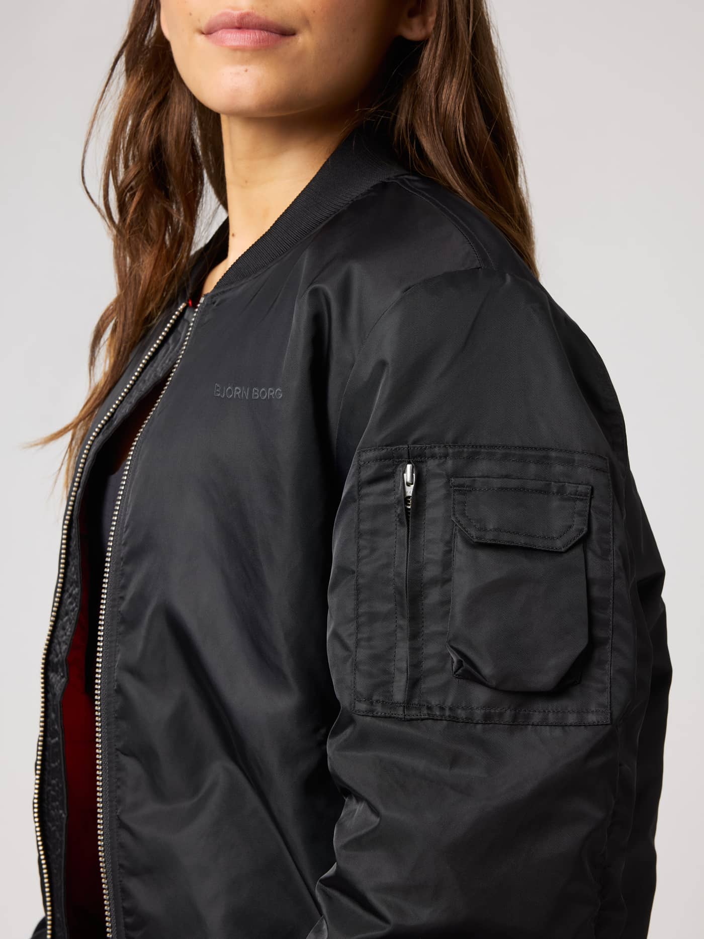 Nærbilde av Studio Bomber Jacket i Black Beauty (Svart) med utility-lomme på ermet, svart logo og tennisdetaljer. - Image 7