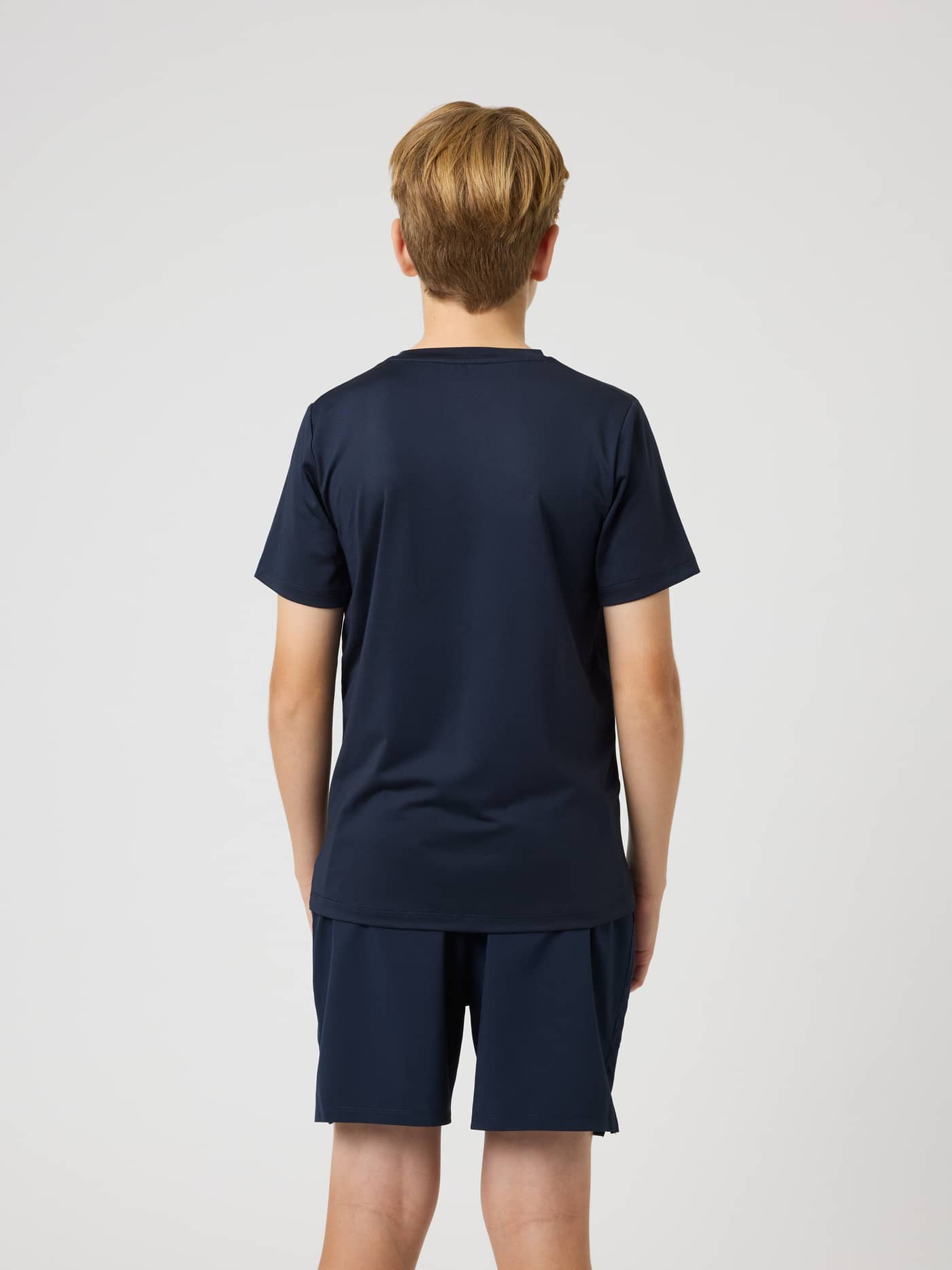Back view of a kid in the Ace Slim T-Shirt in Night sky (Navy), a technical tennis top designed for quick movement. - Image 8