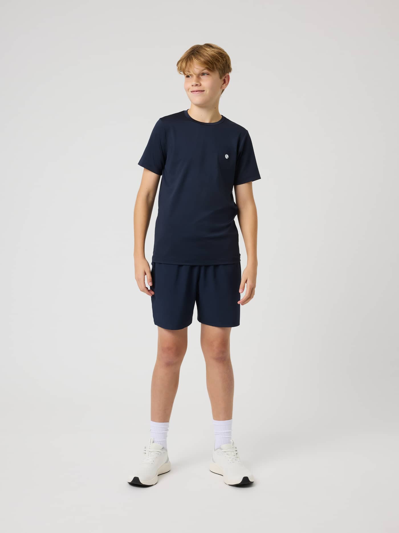 Full-body view of a boy wearing the Ace Slim T-Shirt in Night Sky (Navy), a kids tennis top with a small white logo. - Image 4