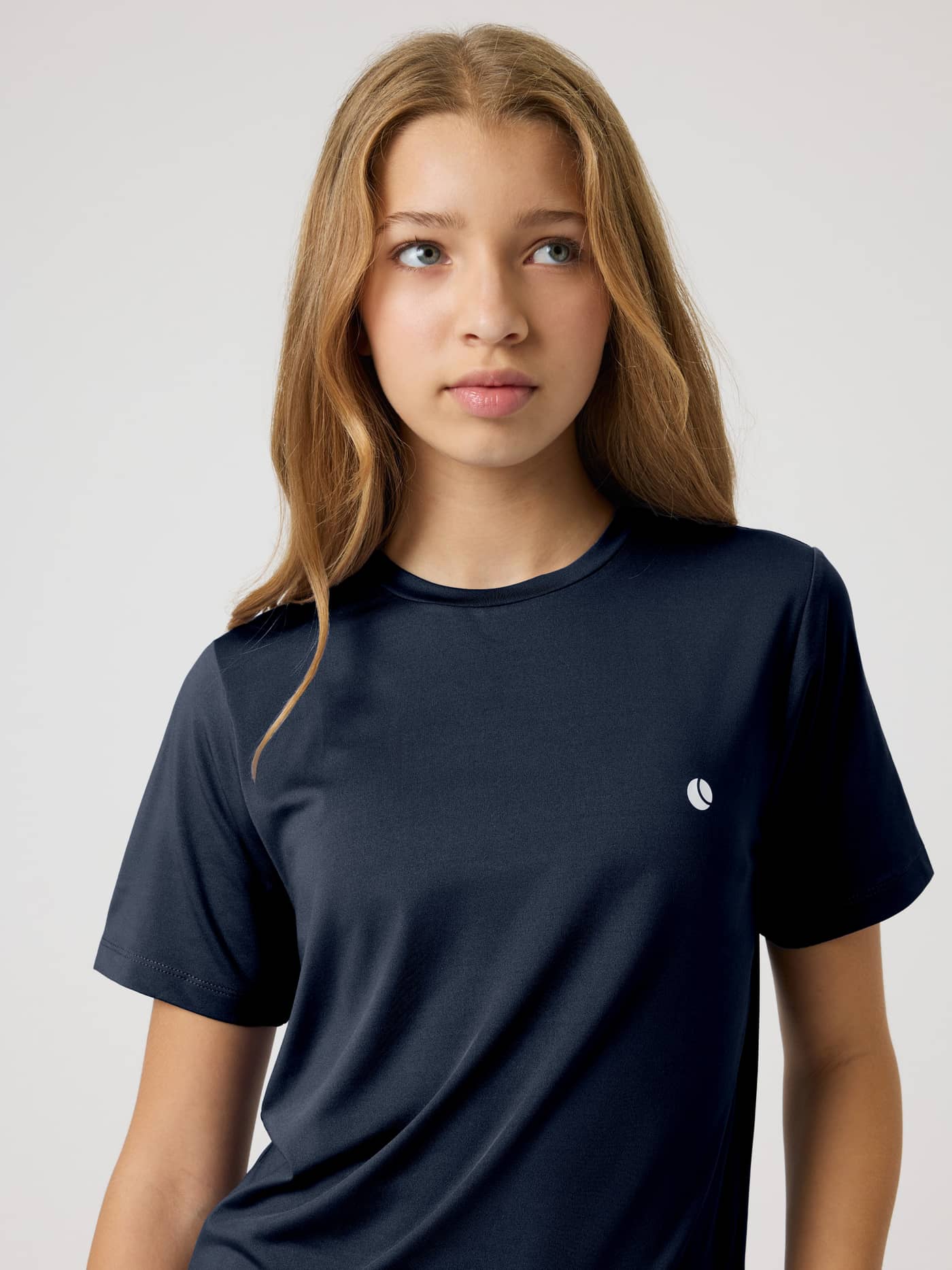 Front view of a model wearing the kids’ Ace Slim T-Shirt in Night sky (Navy) for tennis with a white tennis ball logo. - Image 7