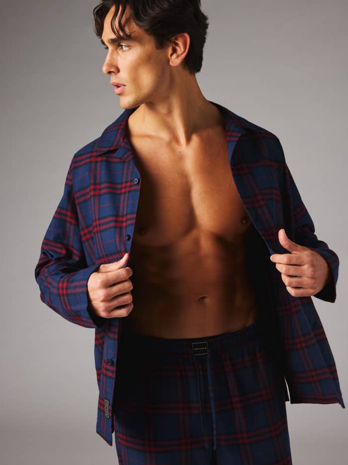 Male model wearing Core Flannel Pyjama Shirt in blue, red, and navy with a tartan pattern for comfortable lounging at home.