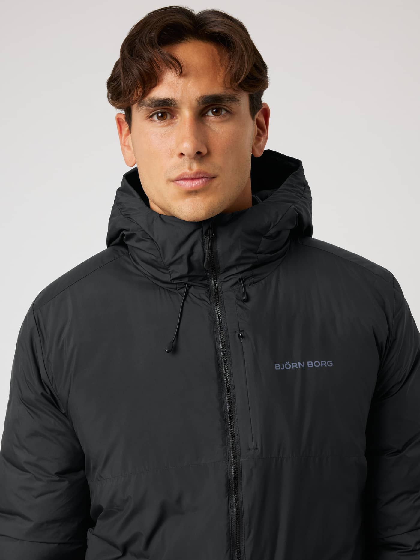 Nærbilde av Borg Liner Hood Jacket i Black Beauty (Svart), vattert trenings- og tennisjakke med grå logo. - Image 5