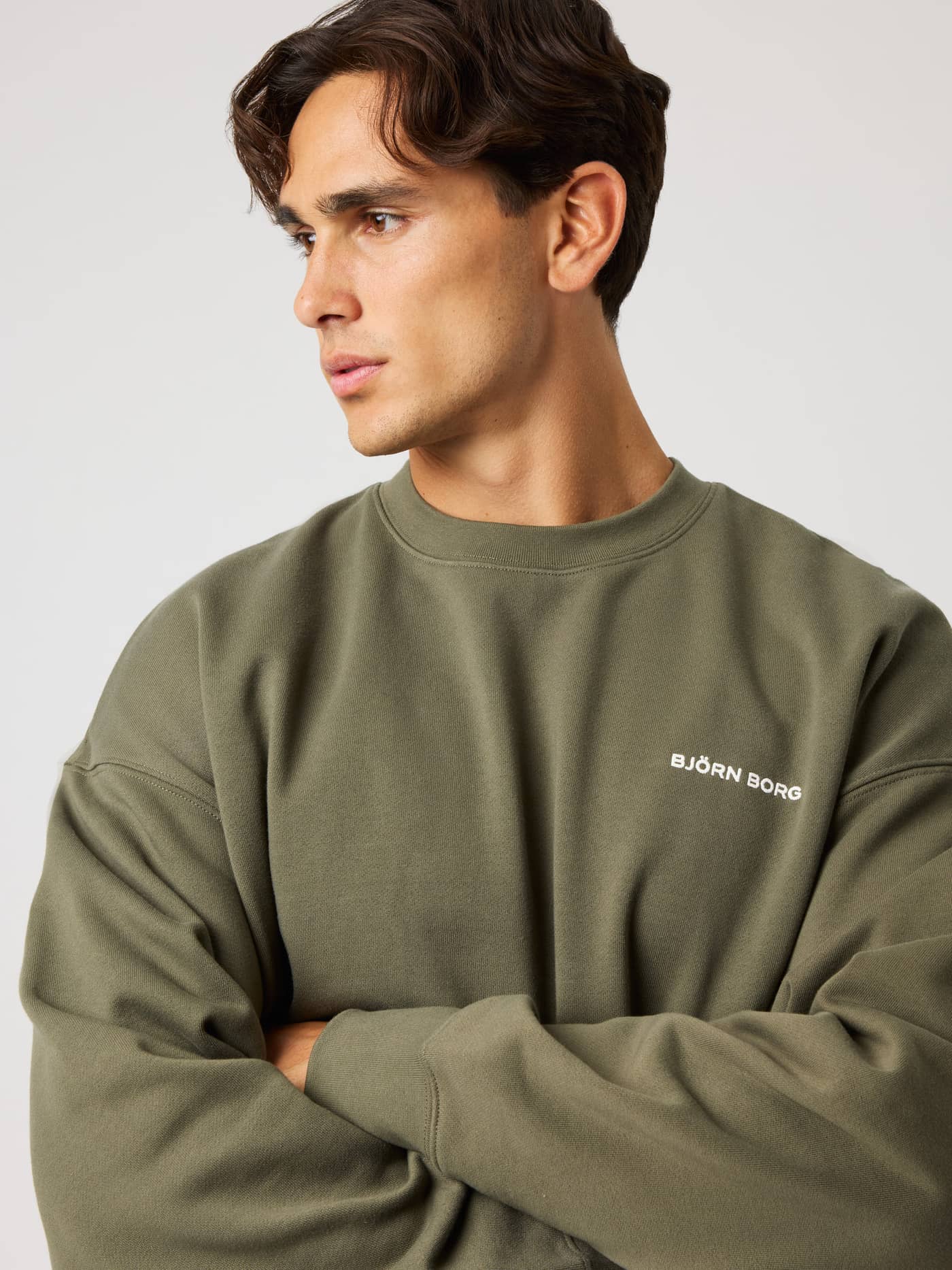 Close-up of a man wearing the Borg Oversized Sweatshirt in Kalamata (Green) with a white logo for training and leisure. - Image 5