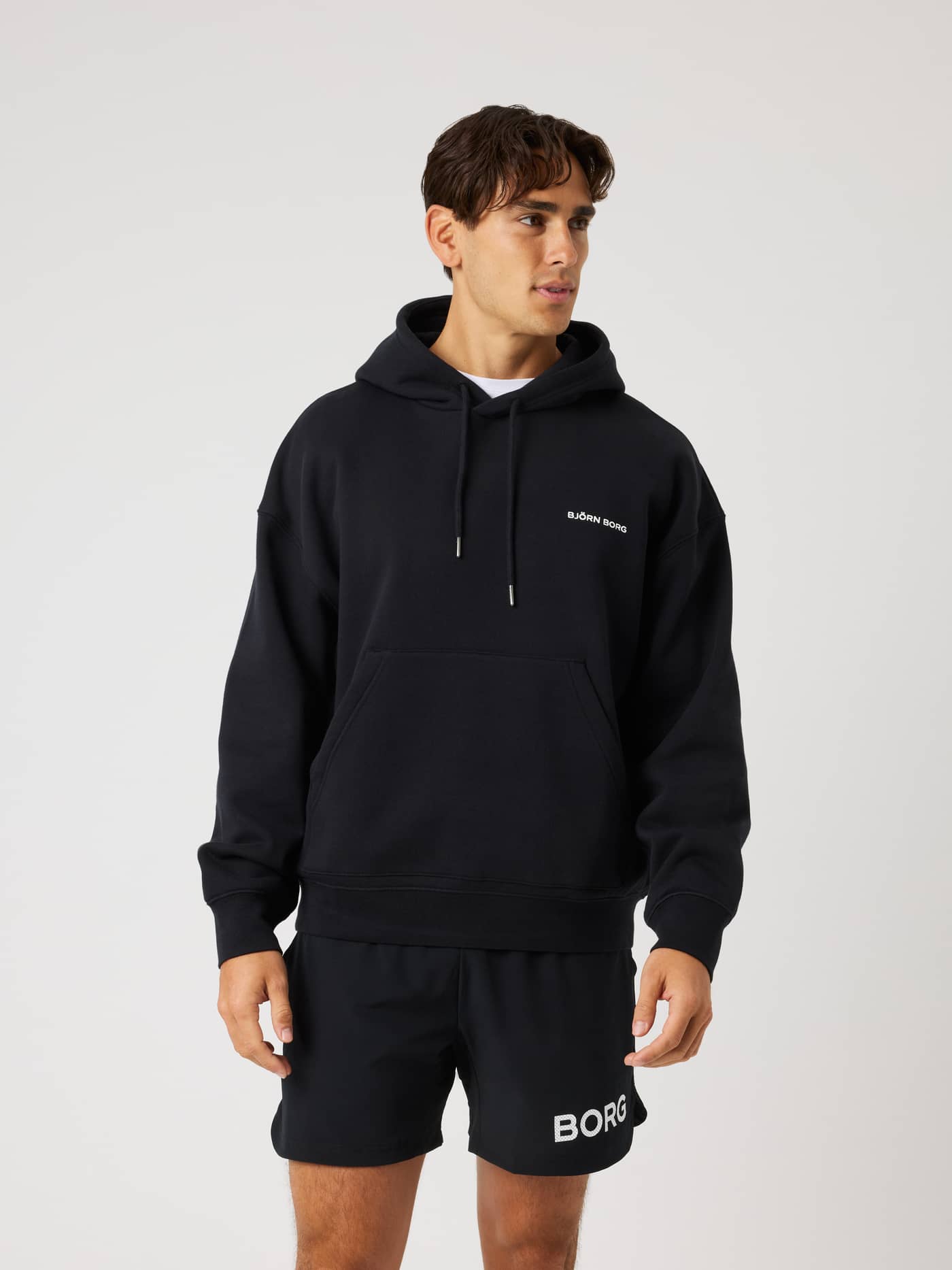 Front view of a man wearing the Borg Oversized Hoodie in Black Beauty (Black) with a white logo for training. - Image 3