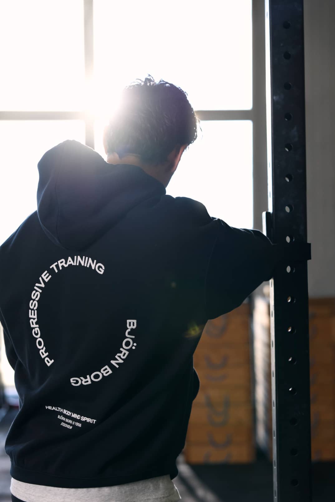 Baksida av Borg Oversized Hoodie i Black Beauty (Svart) med vit grafik i ett gym, perfekt för träning. - Image 1