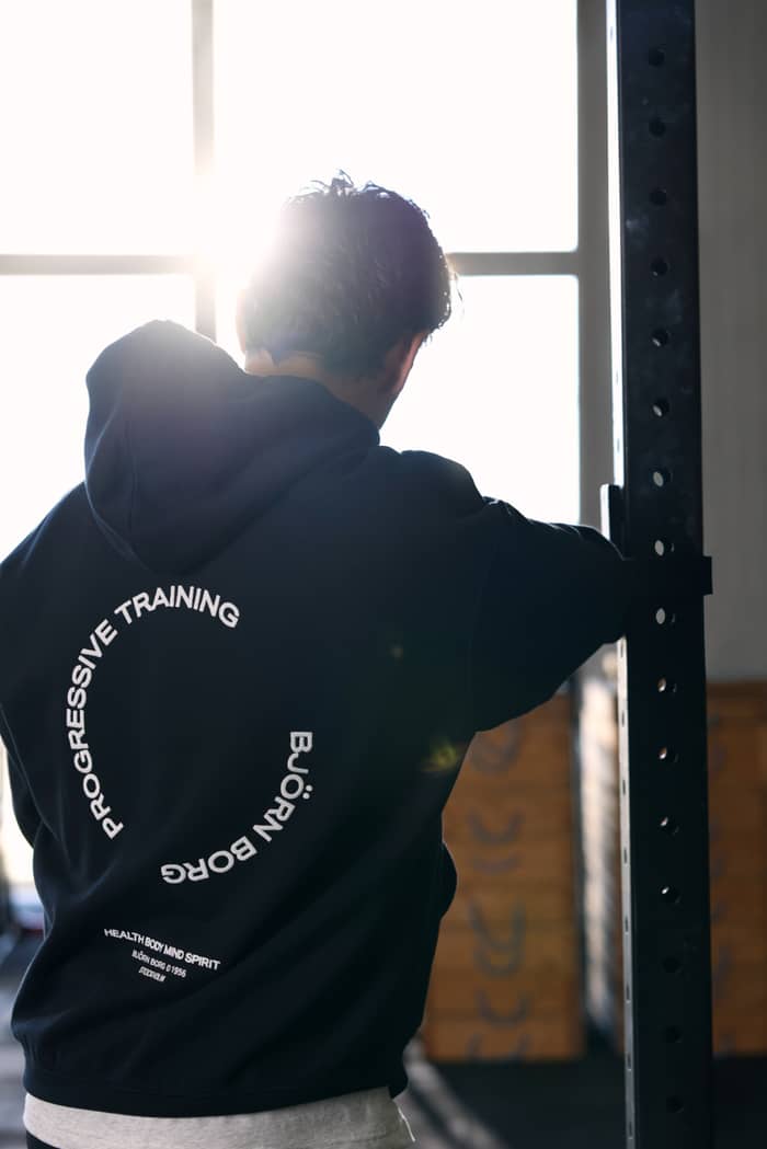 Back view of the Borg Oversized Hoodie in Black Beauty (Black) featuring a white progressive training graphic in a gym.