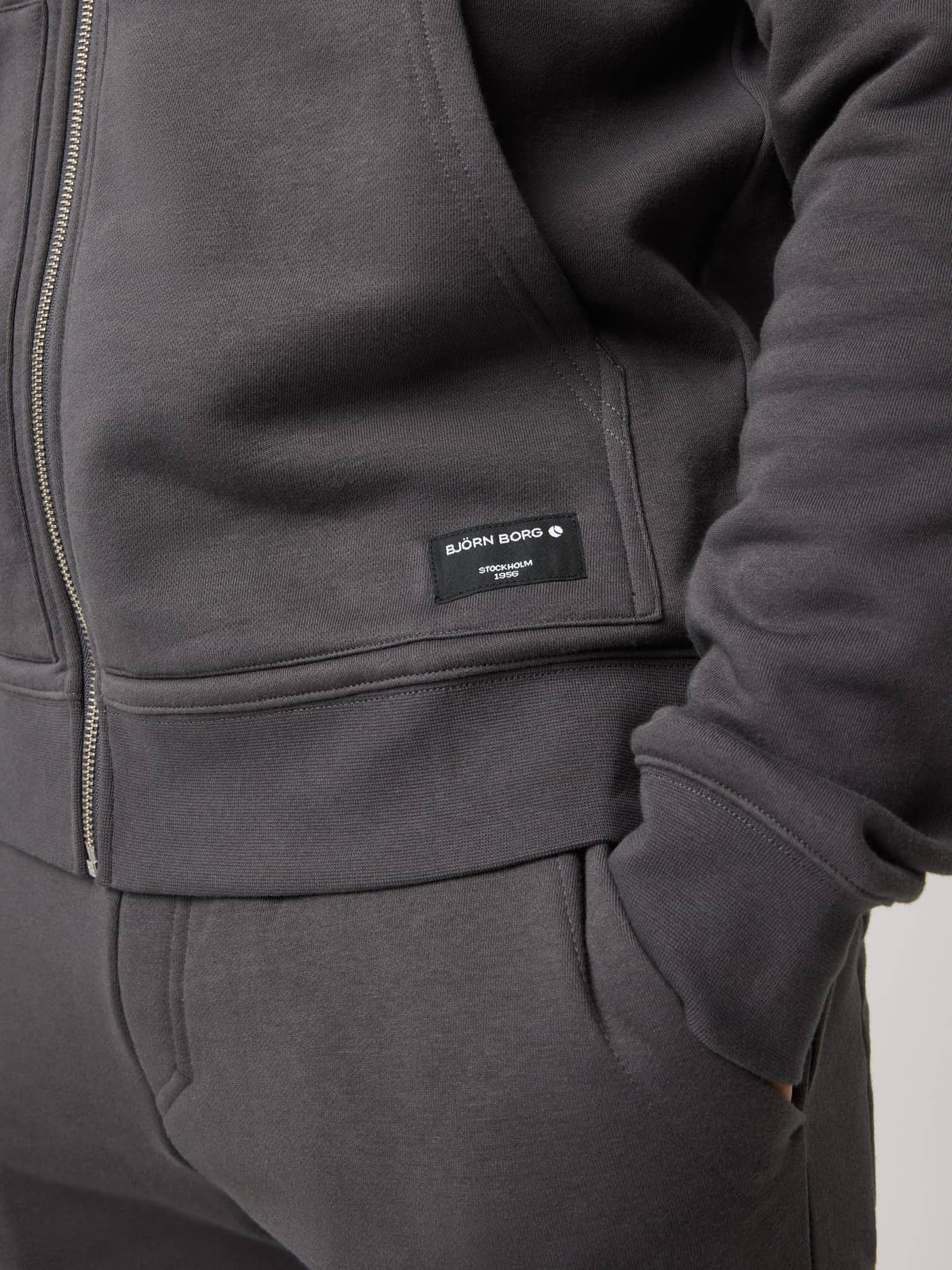 Close-up of the Björn Borg Centre Full Zip Sweatshirt in Asphalt (Black) featuring a black logo label and metal zipper. - Image 5