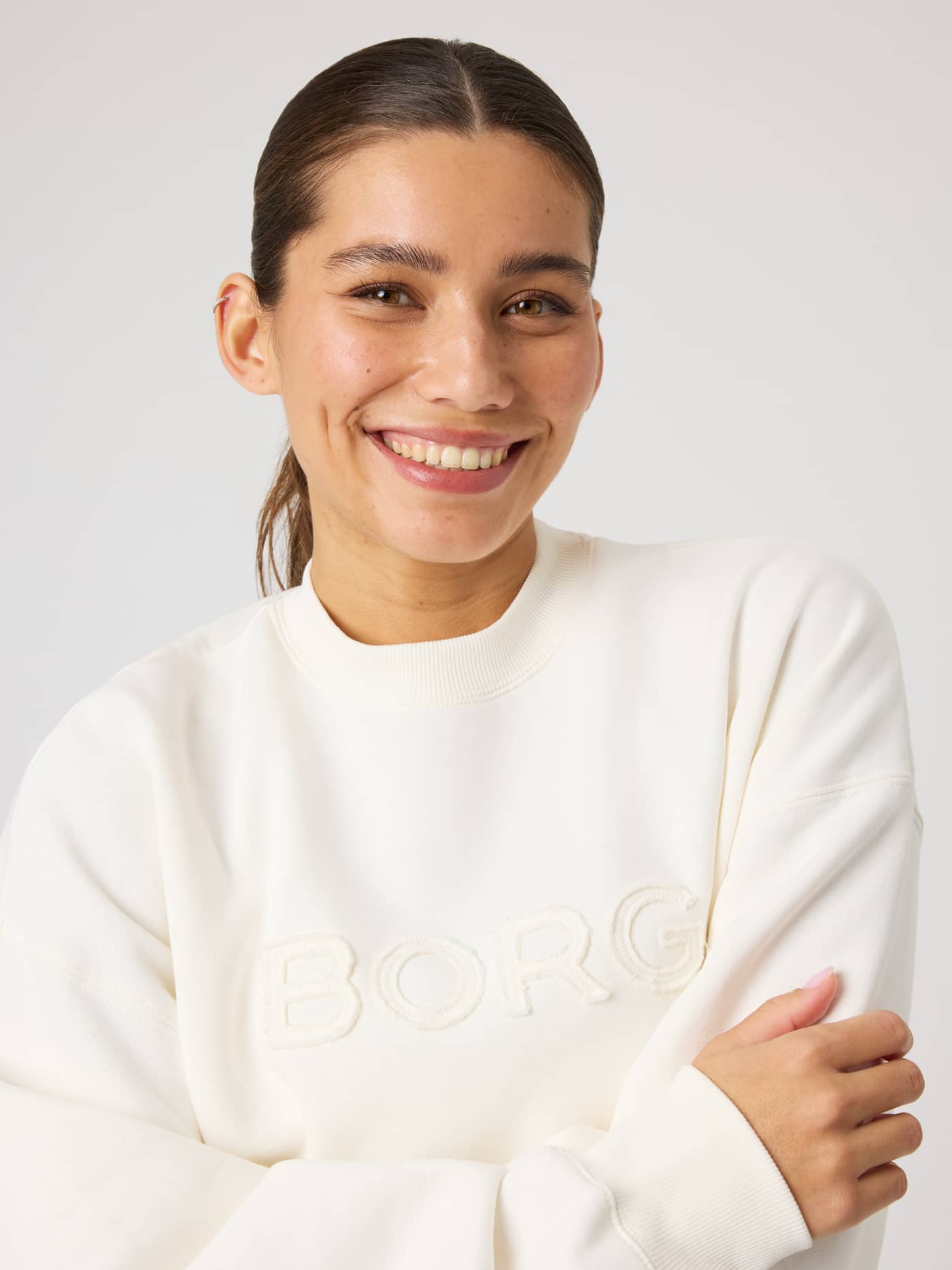 Close-up of a smiling woman in the Studio Oversized Sweatshirt in Tofu (White) with tonal Borg embroidery on the chest. - Image 4