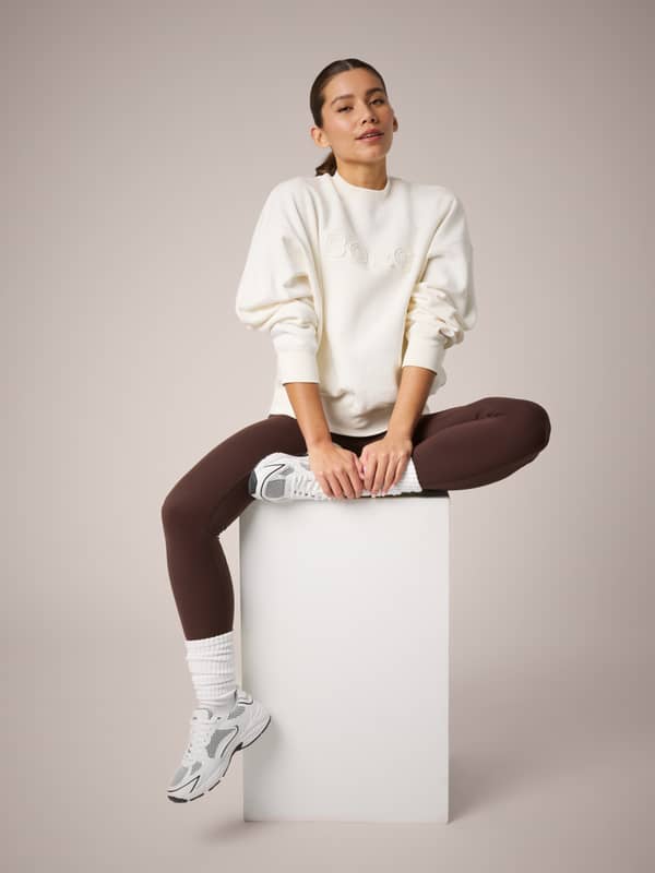 Studio Oversized Sweatshirt in Tofu (Wit) op een zittend model met een oversized pasvorm en tonaal Borg-borduursel.