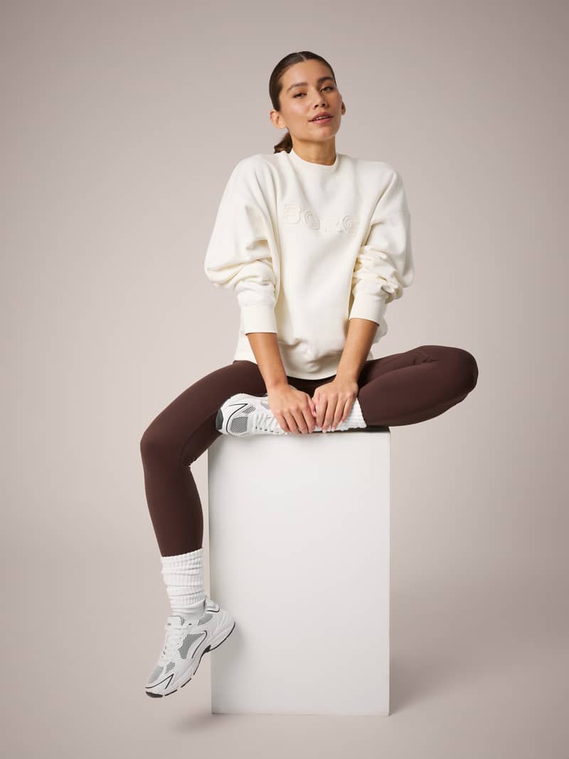 Studio Oversized Sweatshirt in Tofu (White) on a sitting model, featuring a relaxed fit and tonal Borg embroidery.