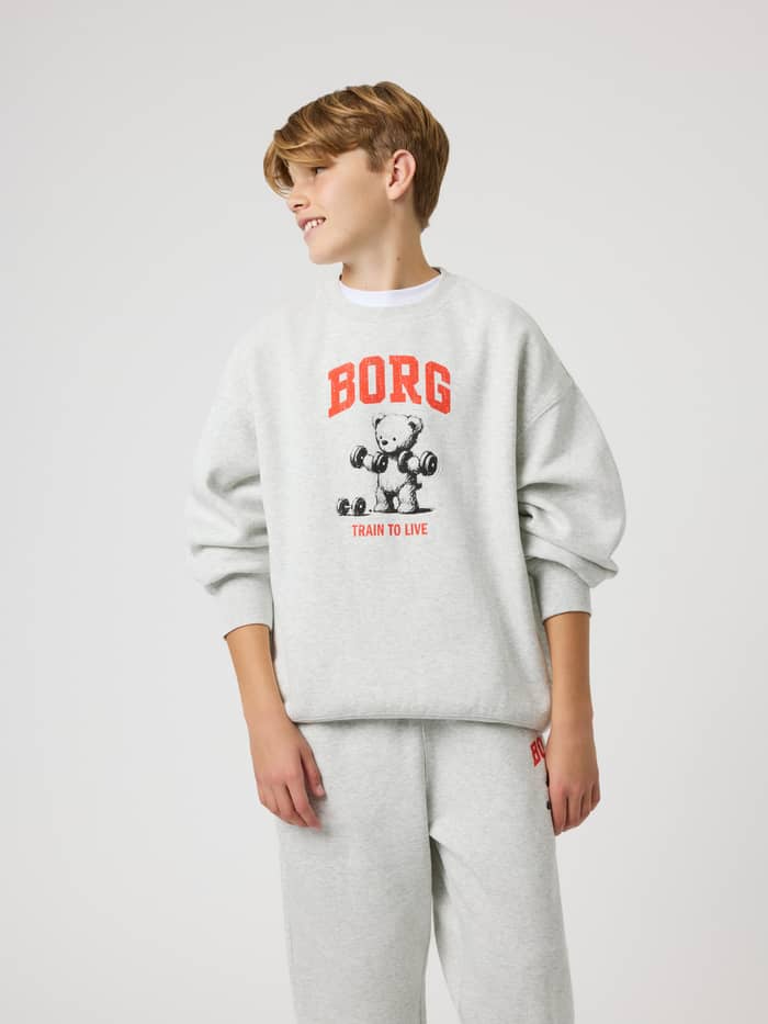 Front view of a model in the kids Borg Oversized Sweatshirt in Ultra Light Grey Melange (Green) with orange training graphic.