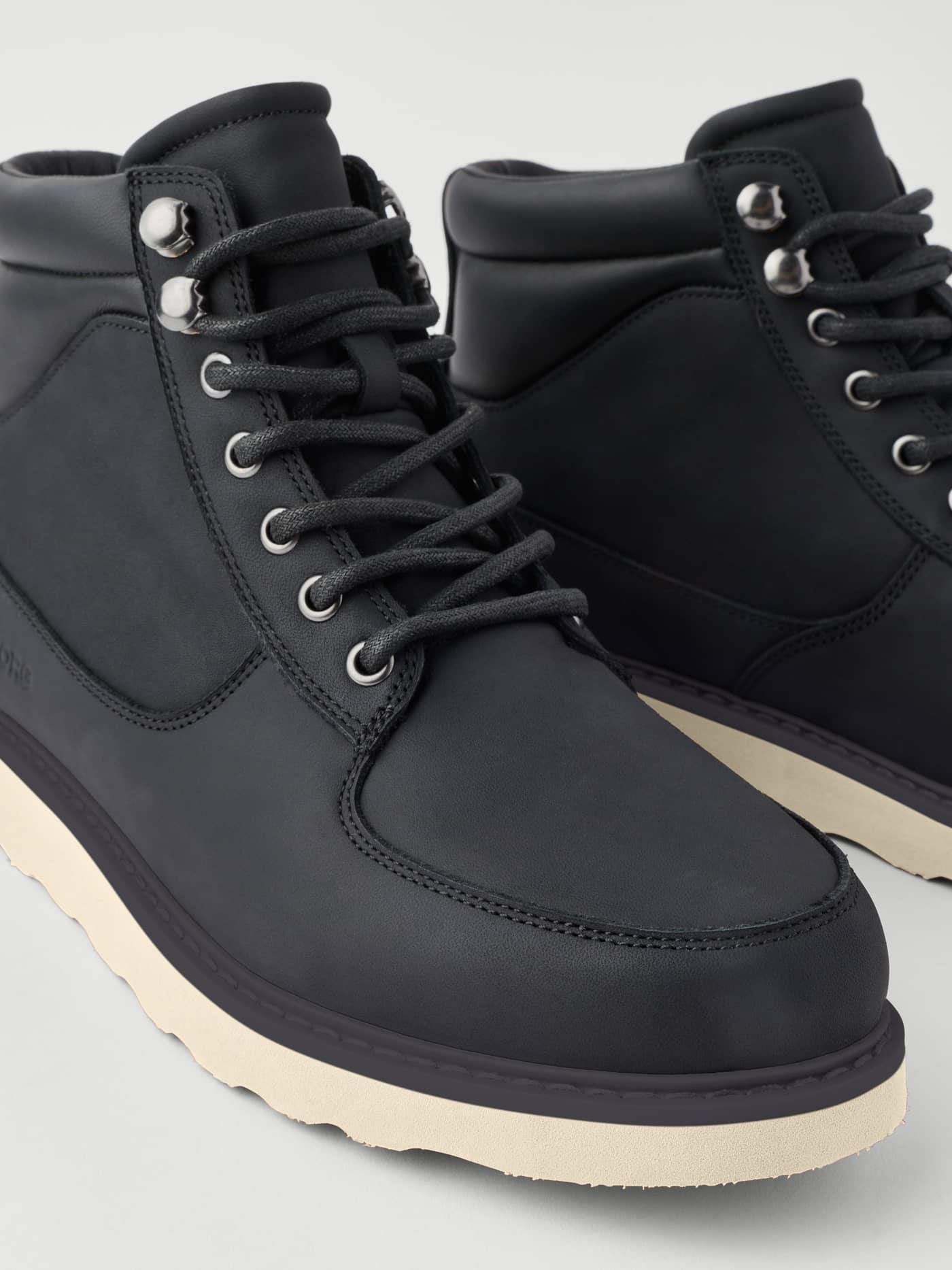 Close-up of the Men's Altitude Boots in Black leather, featuring metal eyelets and a chunky cream sole. - Image 4