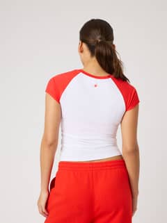 Back view of a model in the Studio Ringer T-Shirt in Brilliant White (White) featuring red raglan sleeves and a tennis logo. - Image 4