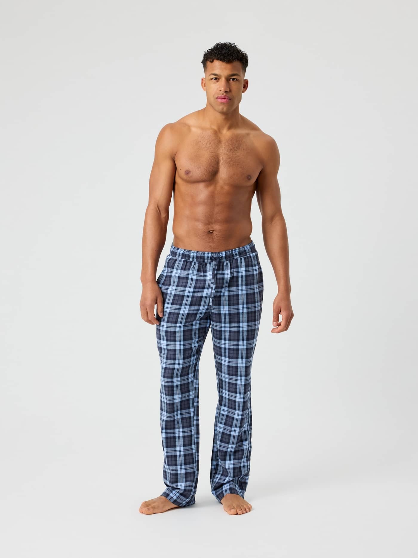 Front view of a model wearing Core Flannel Pyjama Pants in a blue and black check pattern with a drawstring waist. - Image 1