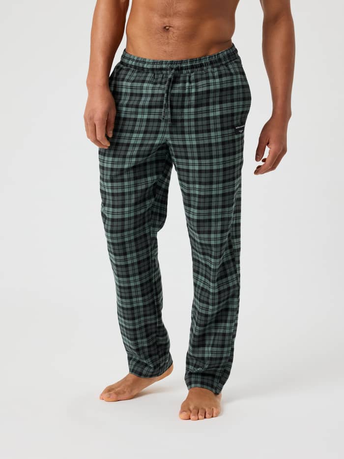 Man wearing Core Flannel Pyjama Pants in green and black check pattern with a drawstring waist and side pockets.