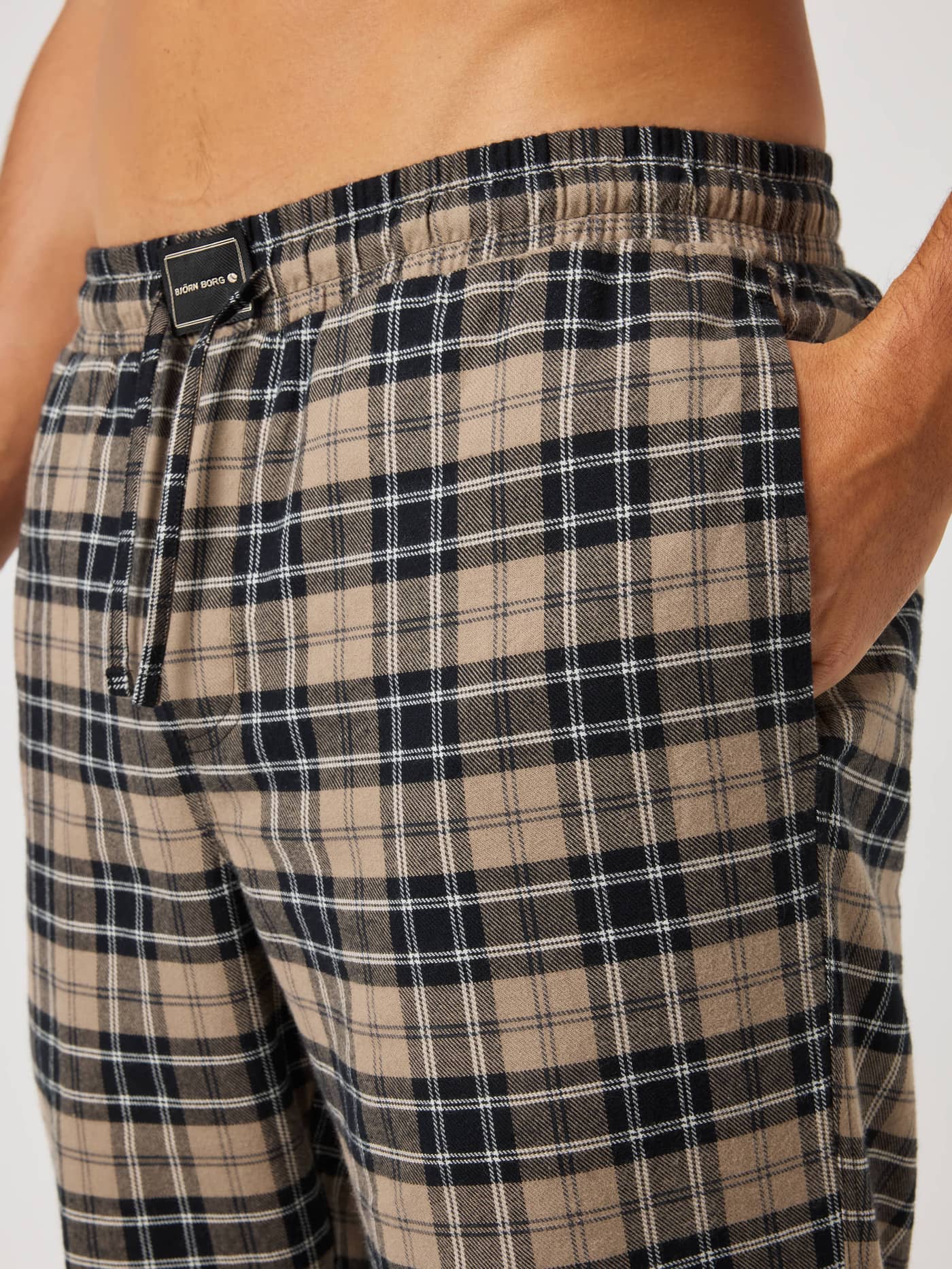 Close-up of Björn Borg Core Flannel Pyjama Pants in beige, black and white tartan with a drawstring and black logo patch. - Image 4