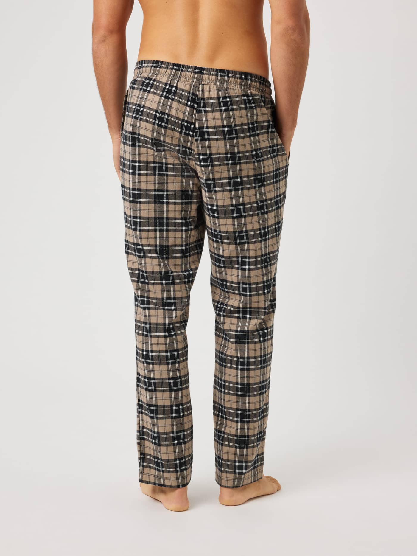 Back view of a model wearing Core Flannel Pyjama Pants in a beige, black, and white Small Tartan 3 check pattern. - Image 2