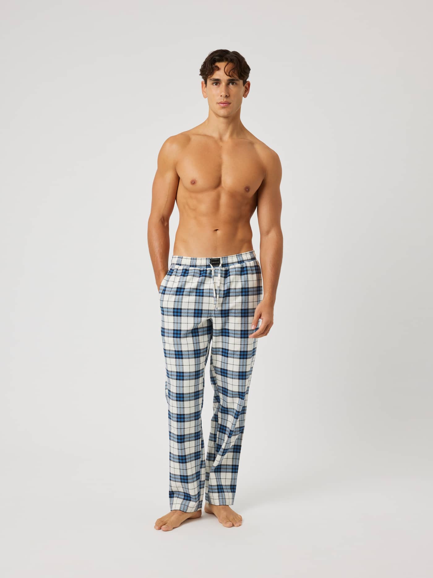Full-body front view of a model wearing Core Flannel Pyjama Pants in a blue, white, and black tartan check pattern. - Image 4