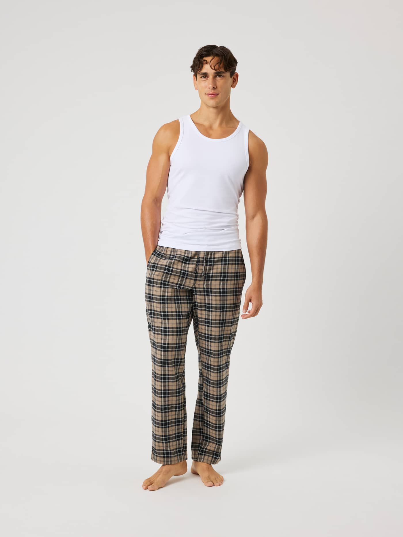 Full-body front view of a model wearing Core Flannel Pyjama Pants in a beige, black, and white tartan pattern. - Image 3