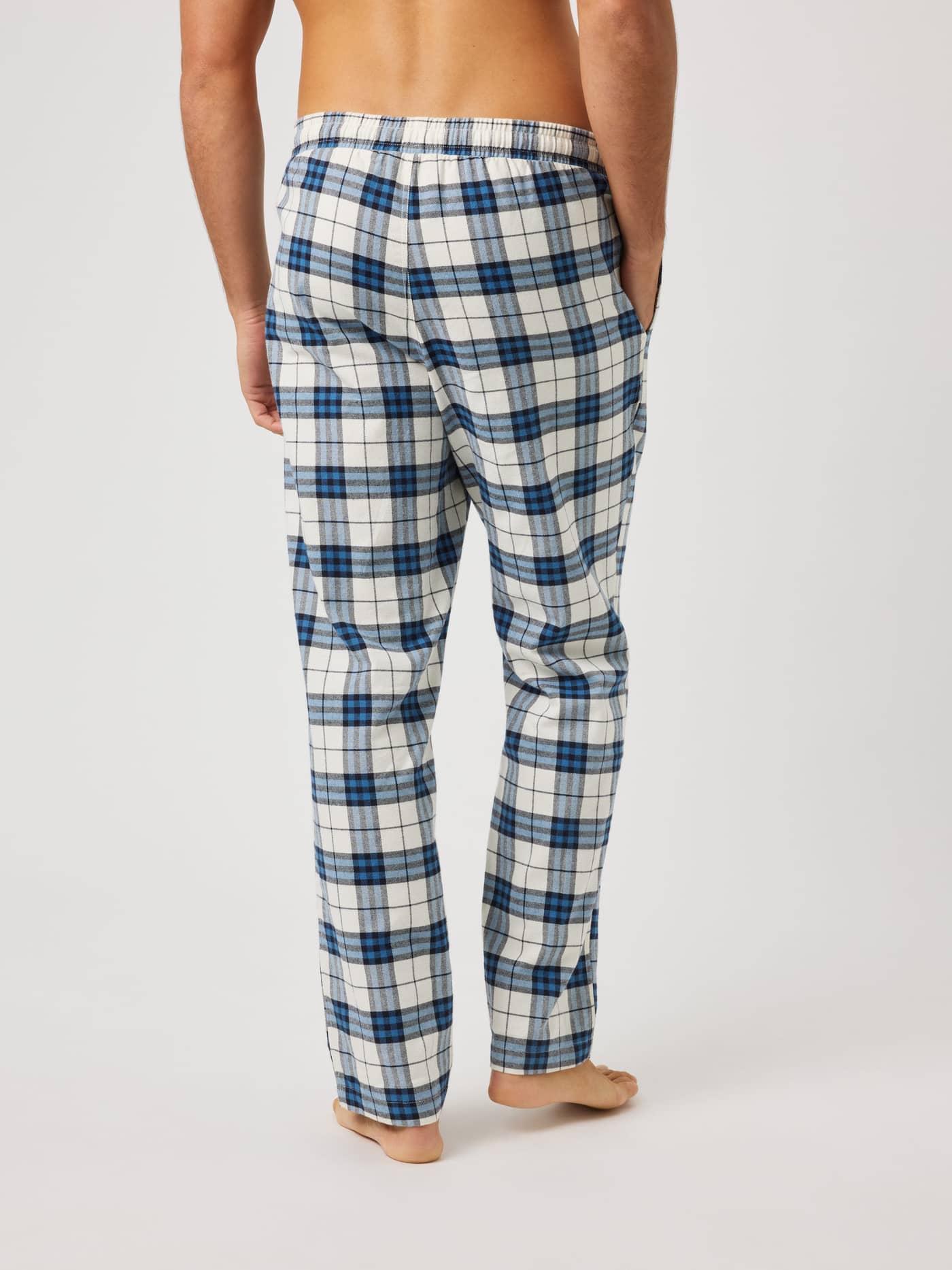 Back view of a man wearing Core Flannel Pyjama Pants in a blue, white, and black tri tartan check pattern. - Image 2