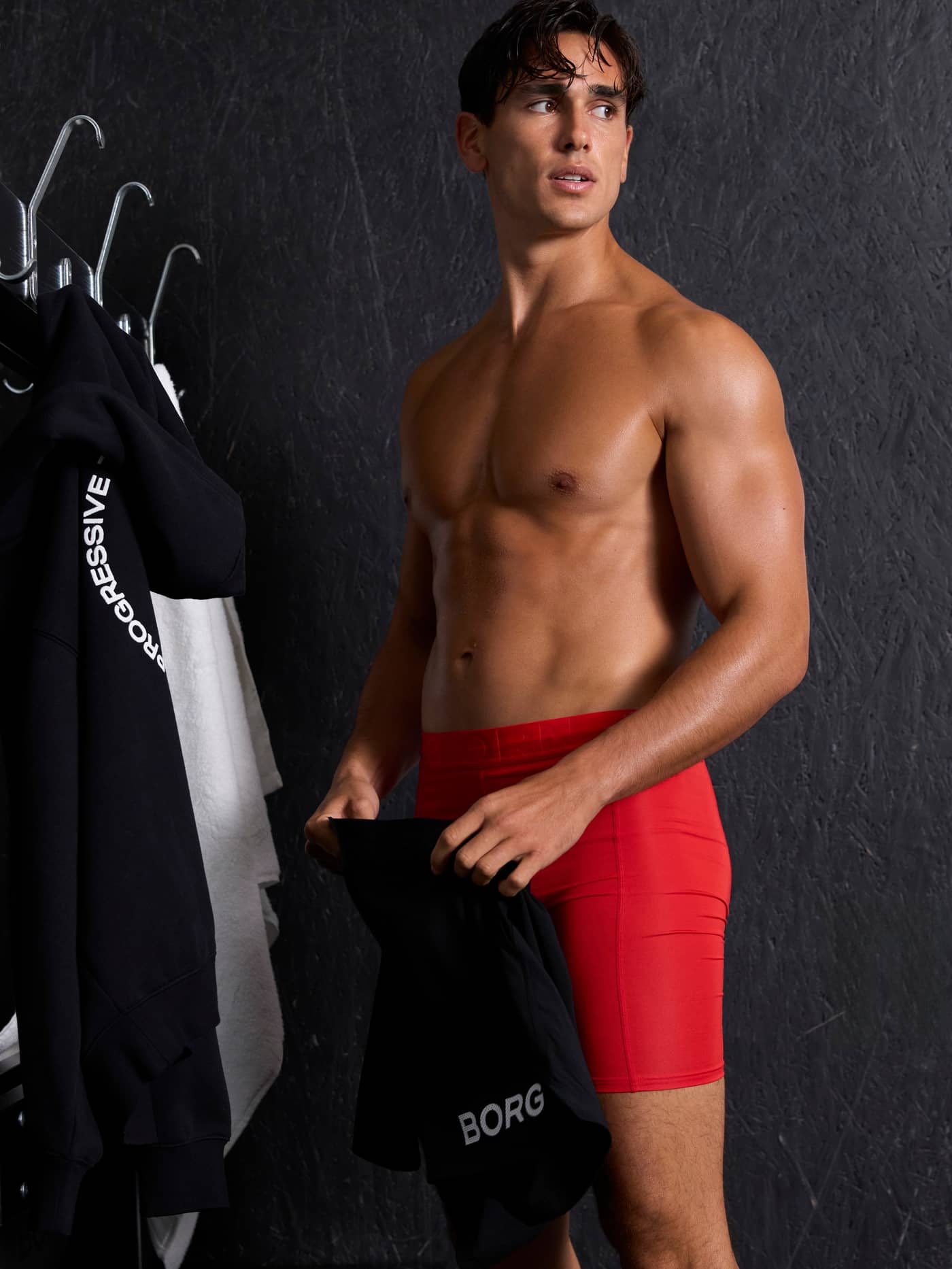 Mannelijk model draagt Sports Lightweight Long Leg Boxers 2-pack in rood en zwart, en houdt een zwart kledingstuk vast. - Image 2