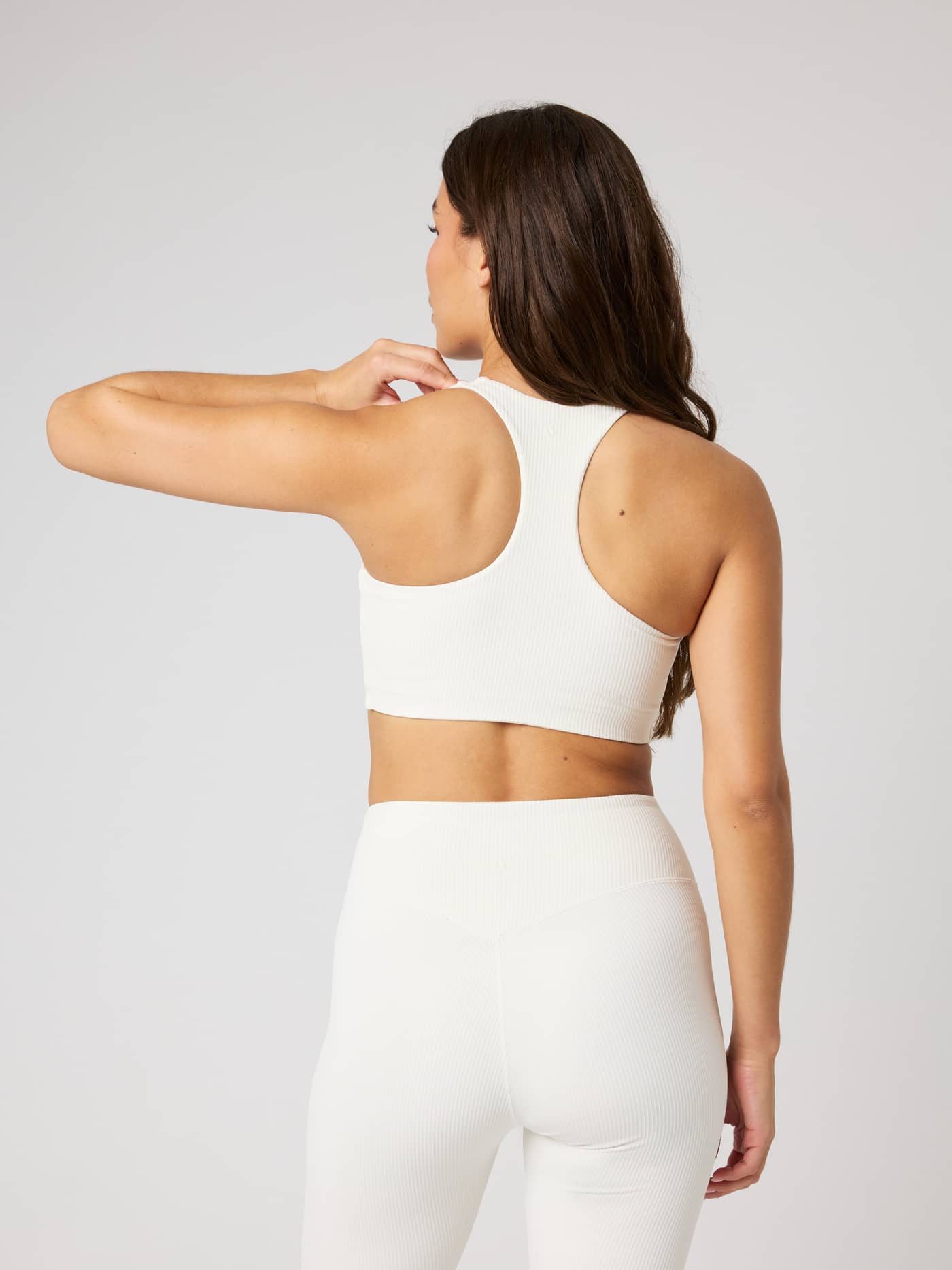 Back view of a model wearing the Studio Ribbed Racerback Bra in Tofu (White) with a ribbed texture for training. - Image 3