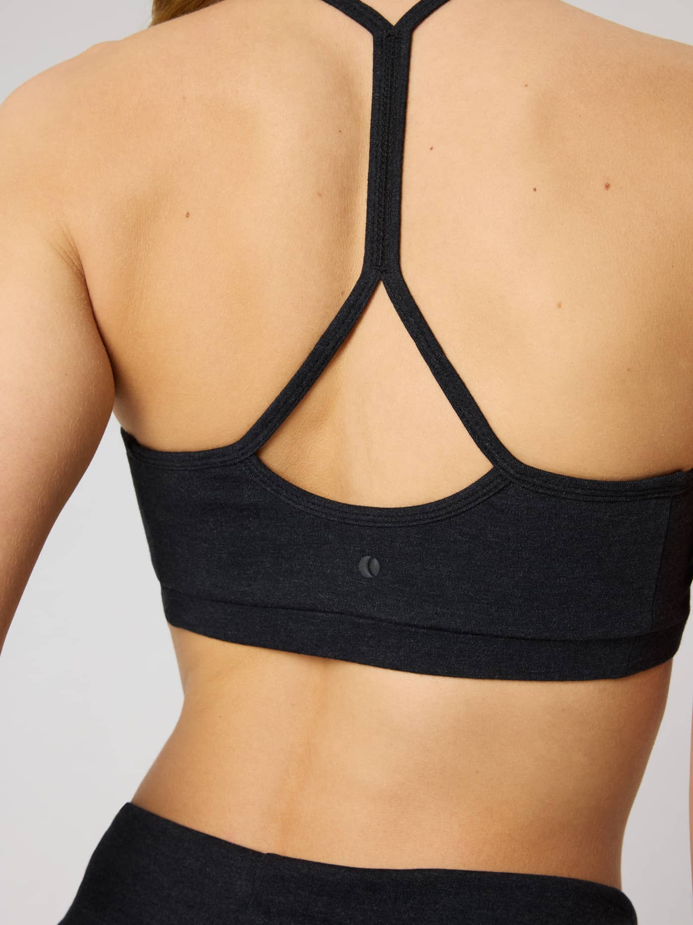 Close-up back view of the Studio Flow Racerback Bra in Black Beauty (Black) with a tonal tennis ball logo for training. - Image 5
