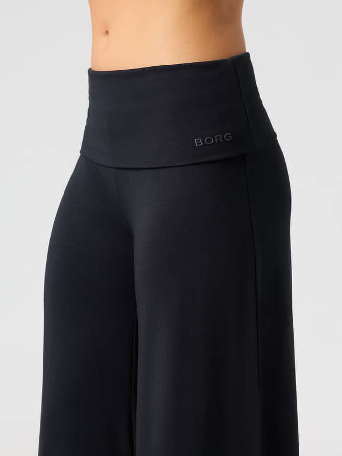 Close-up van de Studio Flow Folded Wide Pants in Black Beauty (zwart) met de omvouwbare tailleband en het tonale logo. - Image 5