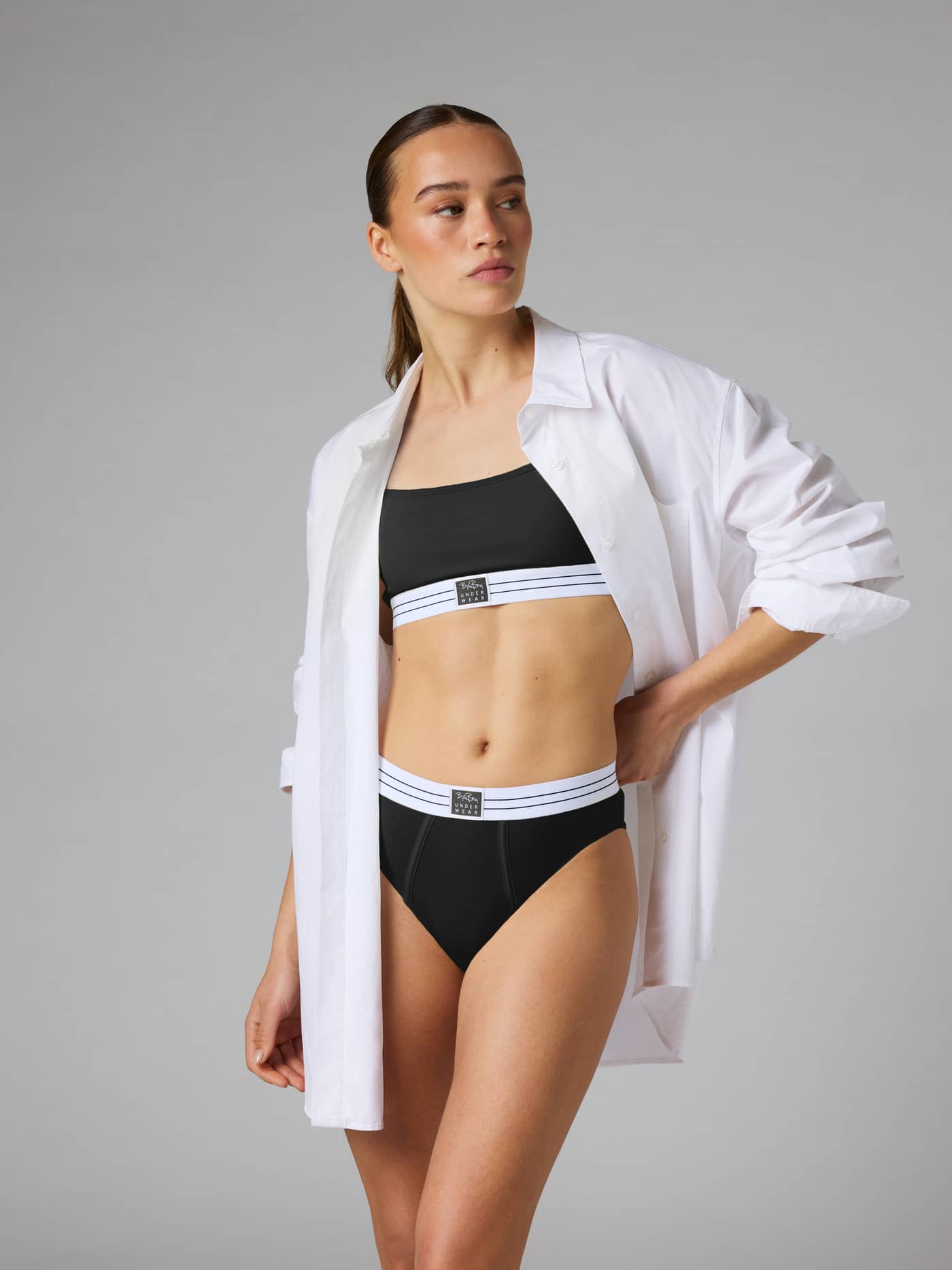 Front view of a model wearing the Original Briefs 2-pack in Black, with a high-waisted fit and striped logo waistband. - Image 2