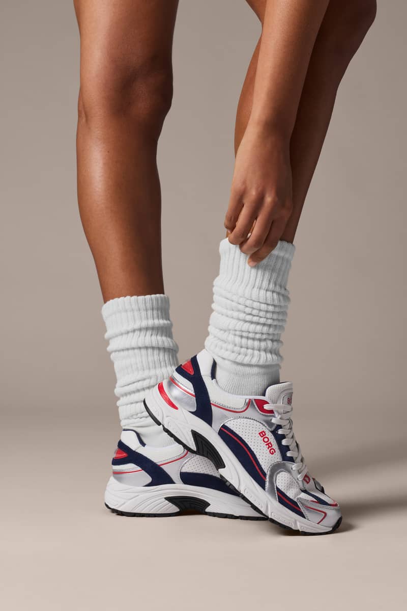 Primer plano de las Women's Alley Sneakers en blanco y azul marino con diseño de inspiración running y calcetines blancos.