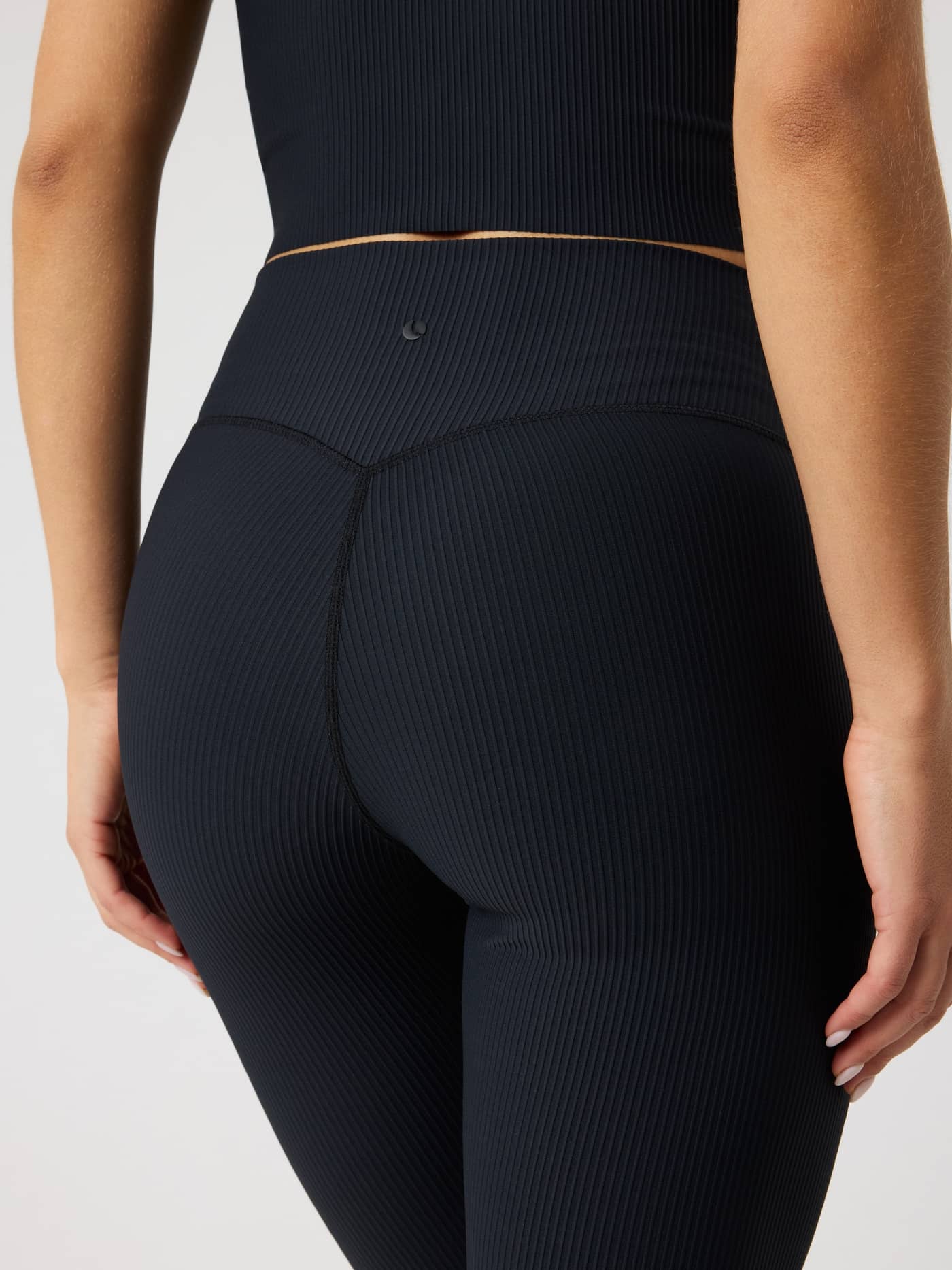 Back view of Studio Ribbed Flare Tights Tall in Black Beauty (Black) with a ribbed training texture and black tennis logo. - Image 4