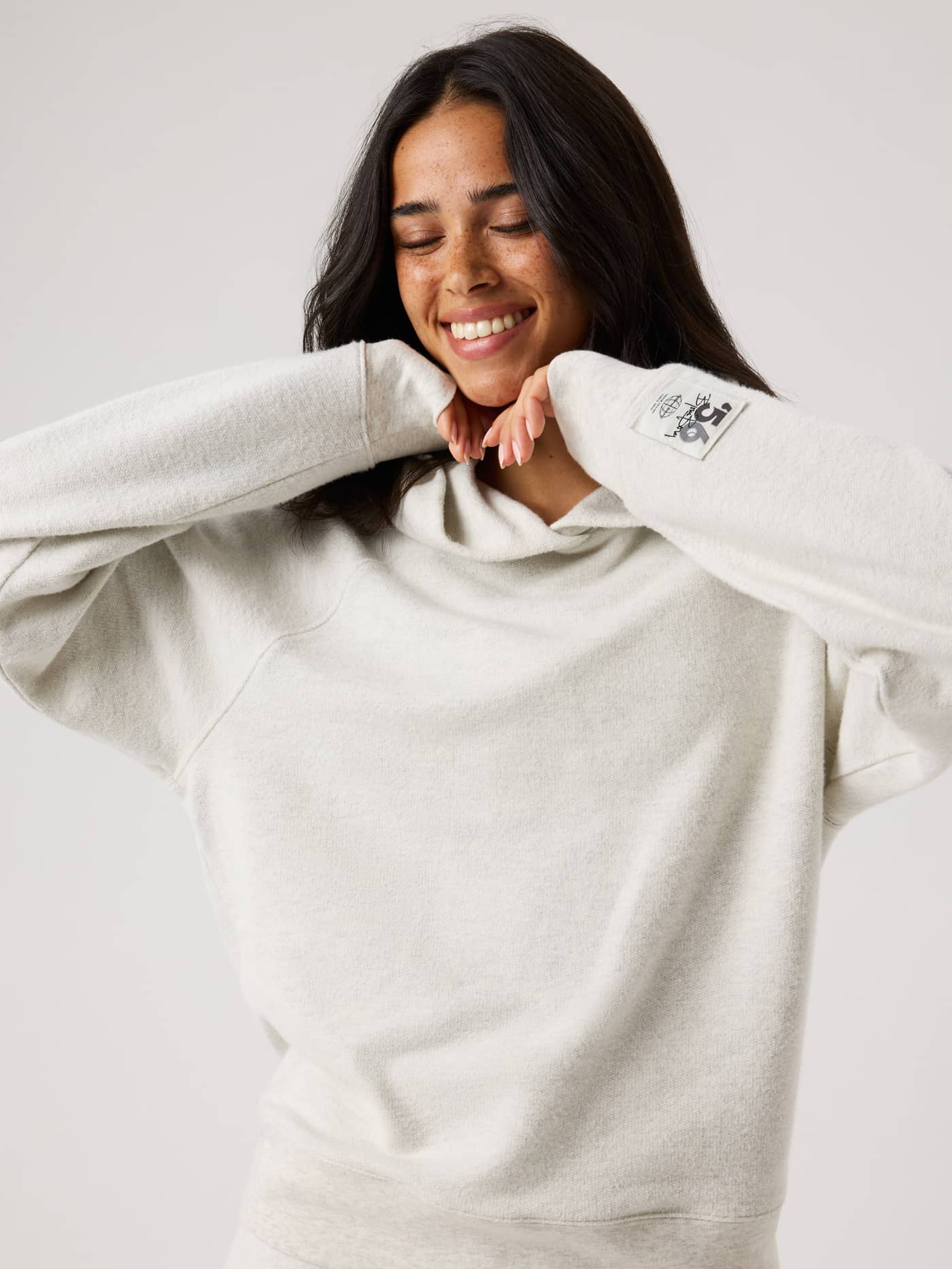 Studio French Terry Oversized Hoodie in Tofu Melange (Beige) with a black logo patch, worn by a woman for tennis warm-ups. - Image 6