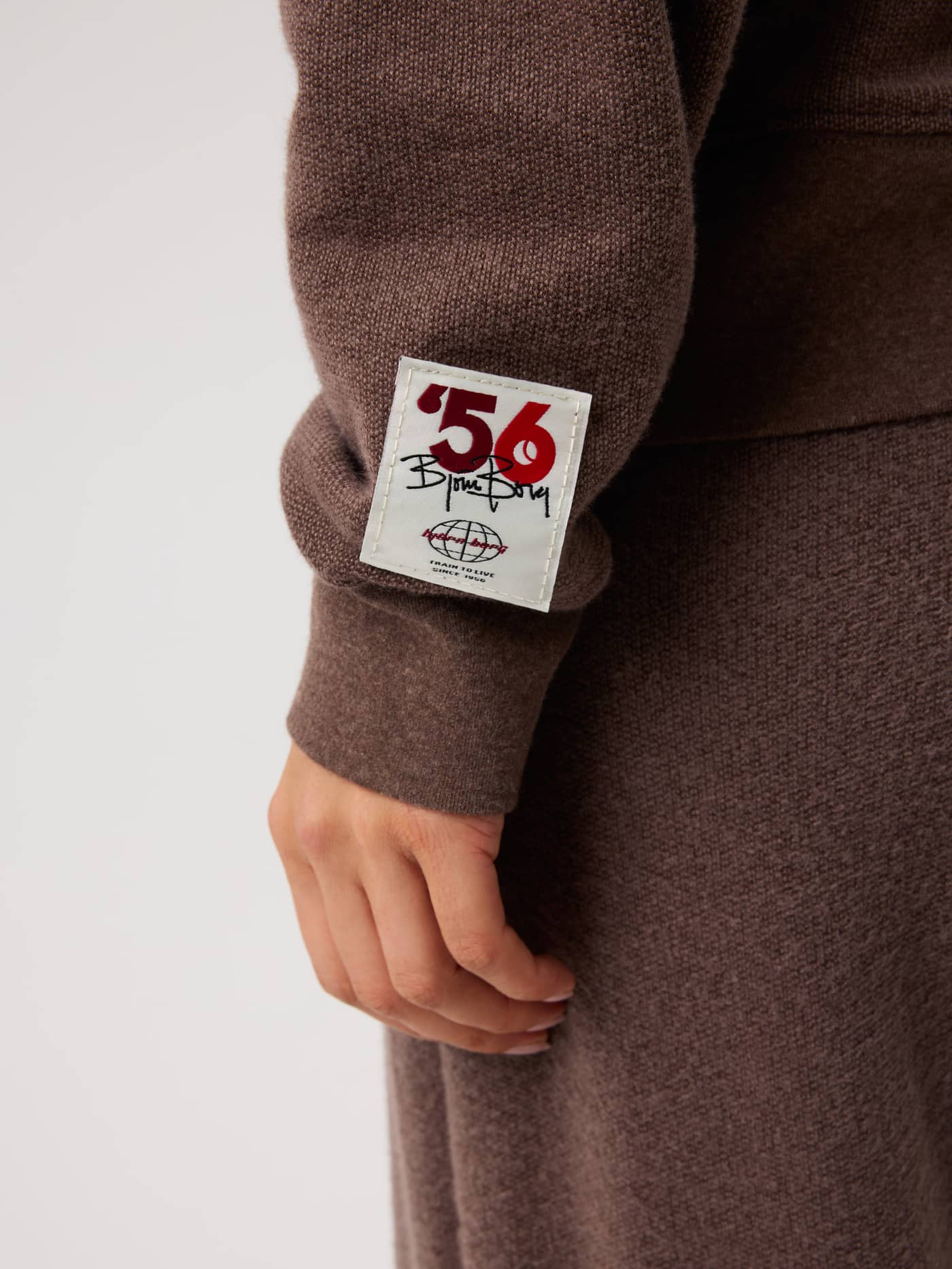 Close-up of the Studio French Terry Oversized Sweatshirt in Brown Melange (Brown) with a white heritage tennis logo patch. - Image 5