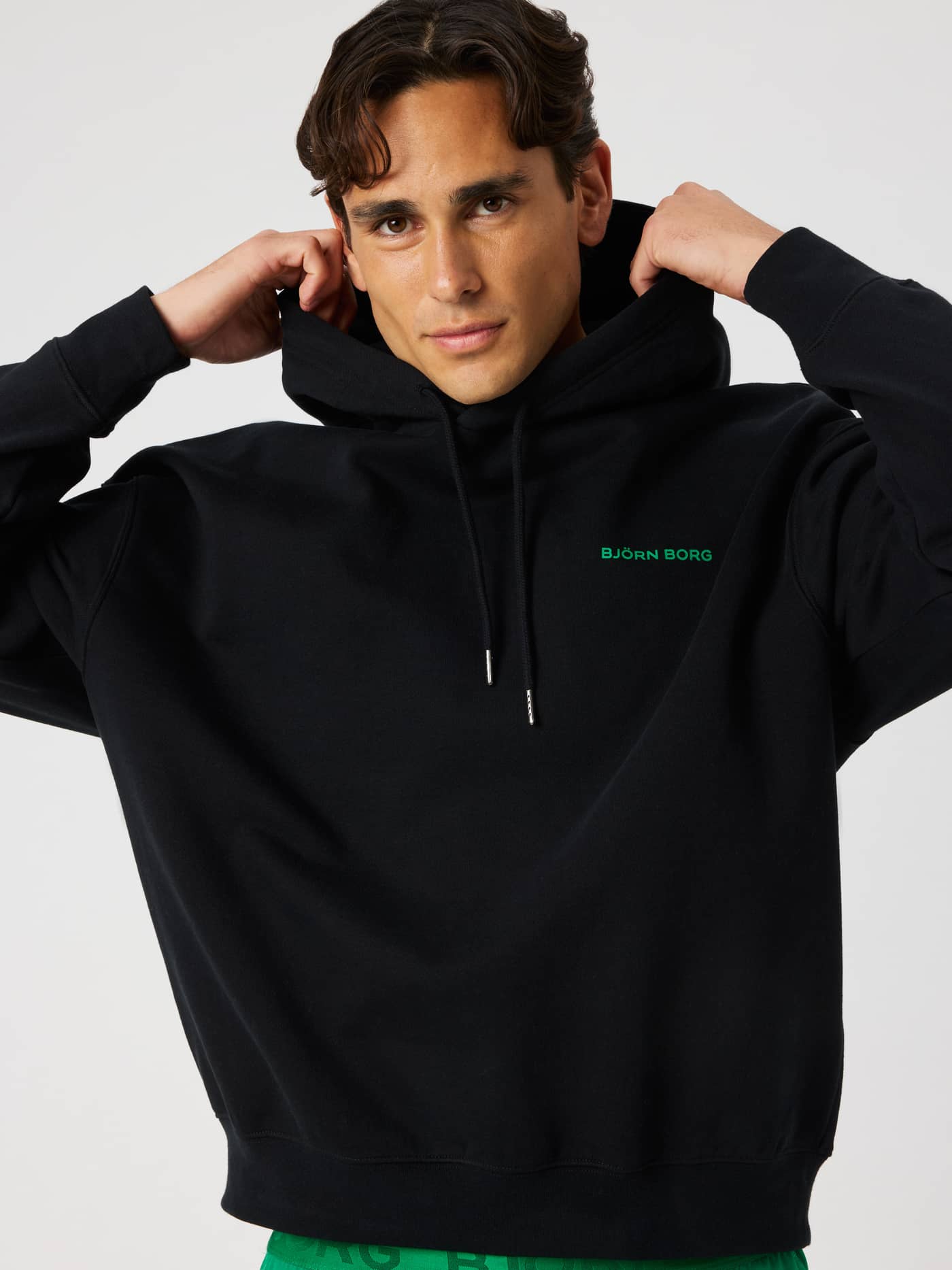 Close-up of the Borg Oversized Hoodie in Black Beauty (black) featuring a green logo print and drawstring hood. - Image 6