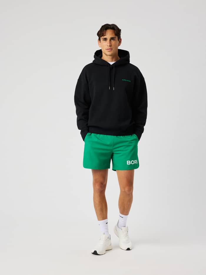 Front view of a male model wearing the Borg Oversized Hoodie in Black Beauty (black) with a green logo.