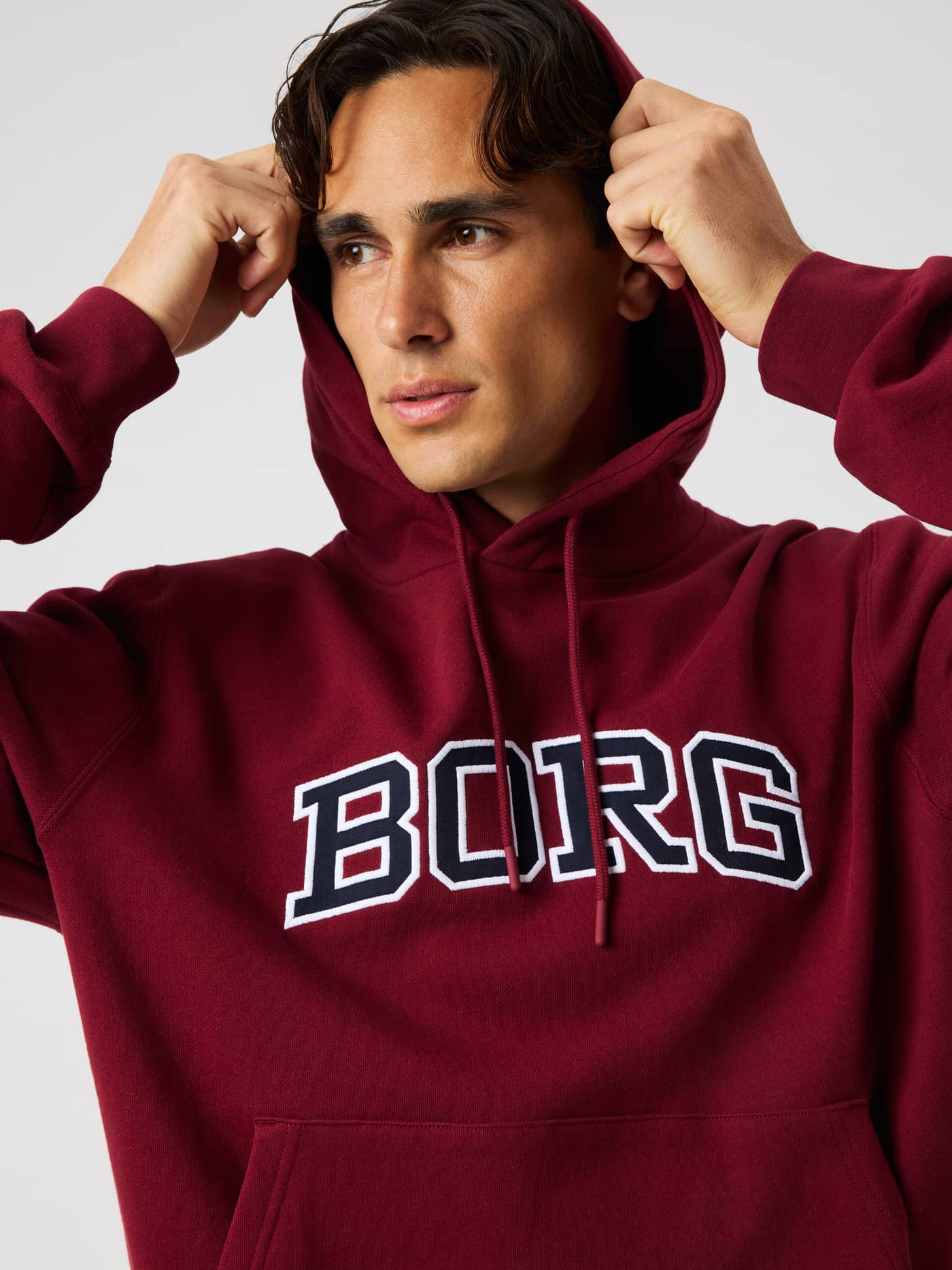 Close-up of a model wearing the Borg Classic Print Hoodie in Cabernet (Red) featuring a large white BORG logo on the chest. - Image 4