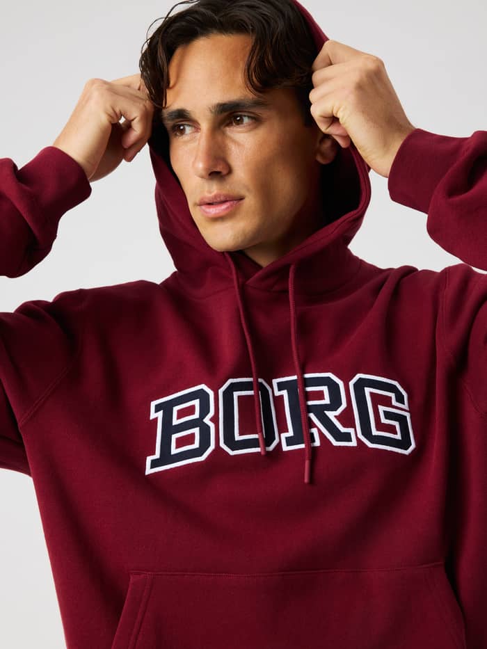 Close-up of a model wearing the Borg Classic Print Hoodie in Cabernet (Red) featuring a large white BORG logo on the chest.